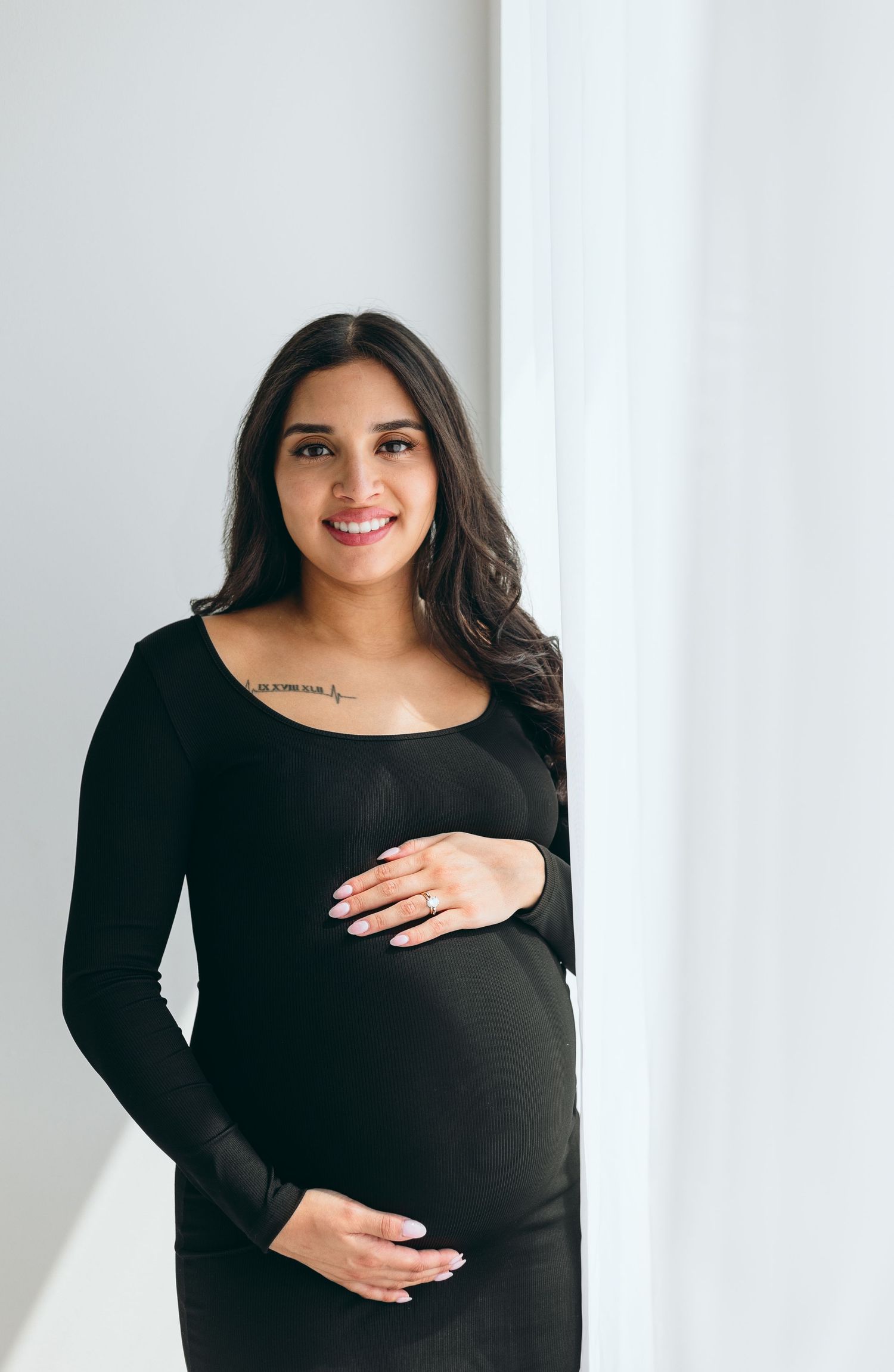 Maternity portraits of woman in black dress against white backdrop.