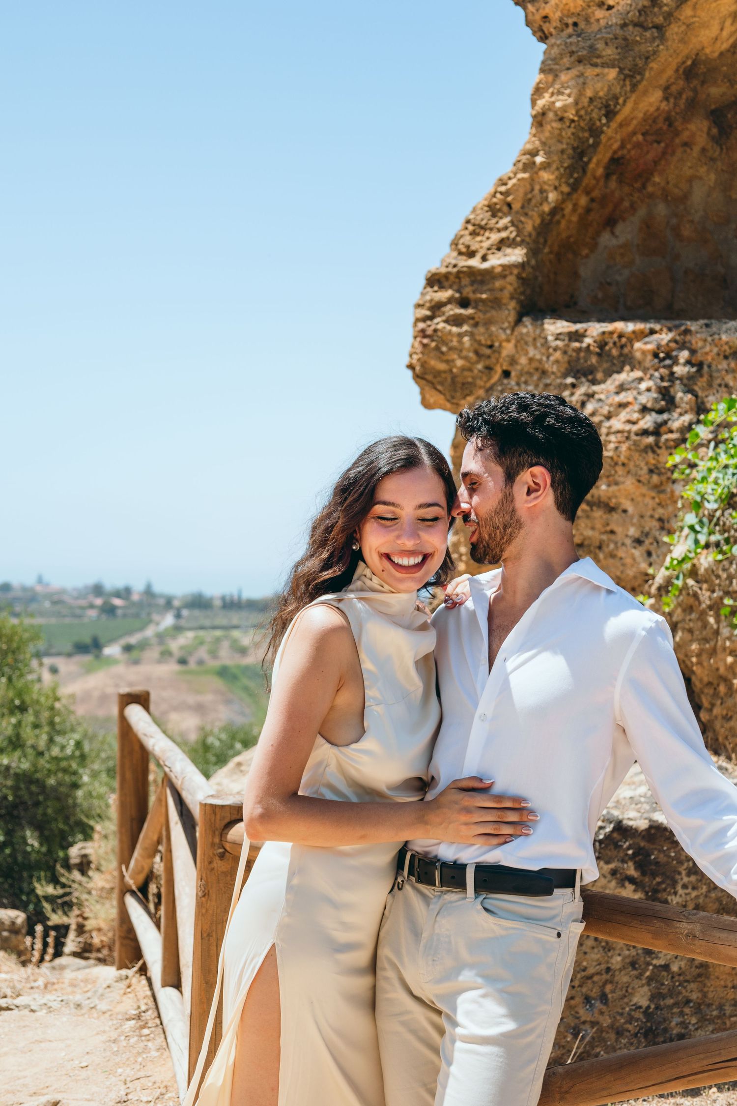 A candid moment of laughter and embrace against rocky cliffs and blue skies.