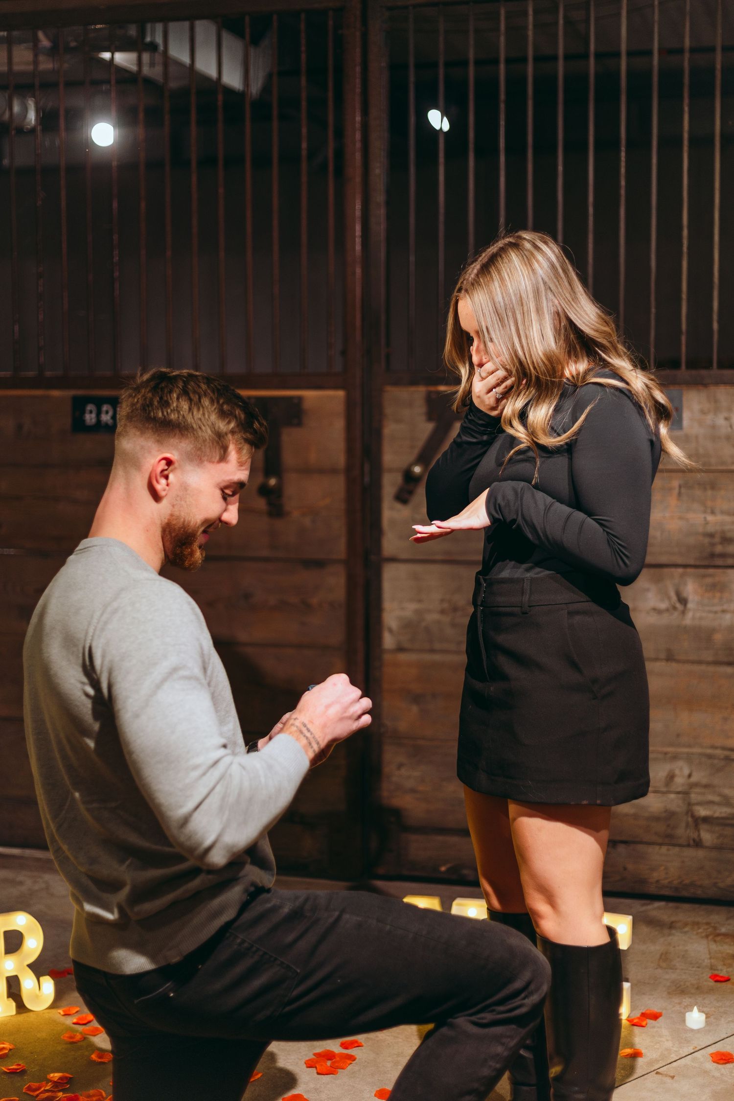 A proposal moment captured in a rustic setting with glowing letters and wooden walls.
