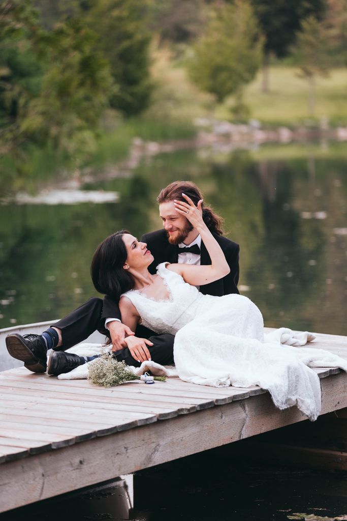 Joyful wedding couple shares a playful moment while lying on a dock near a lake.