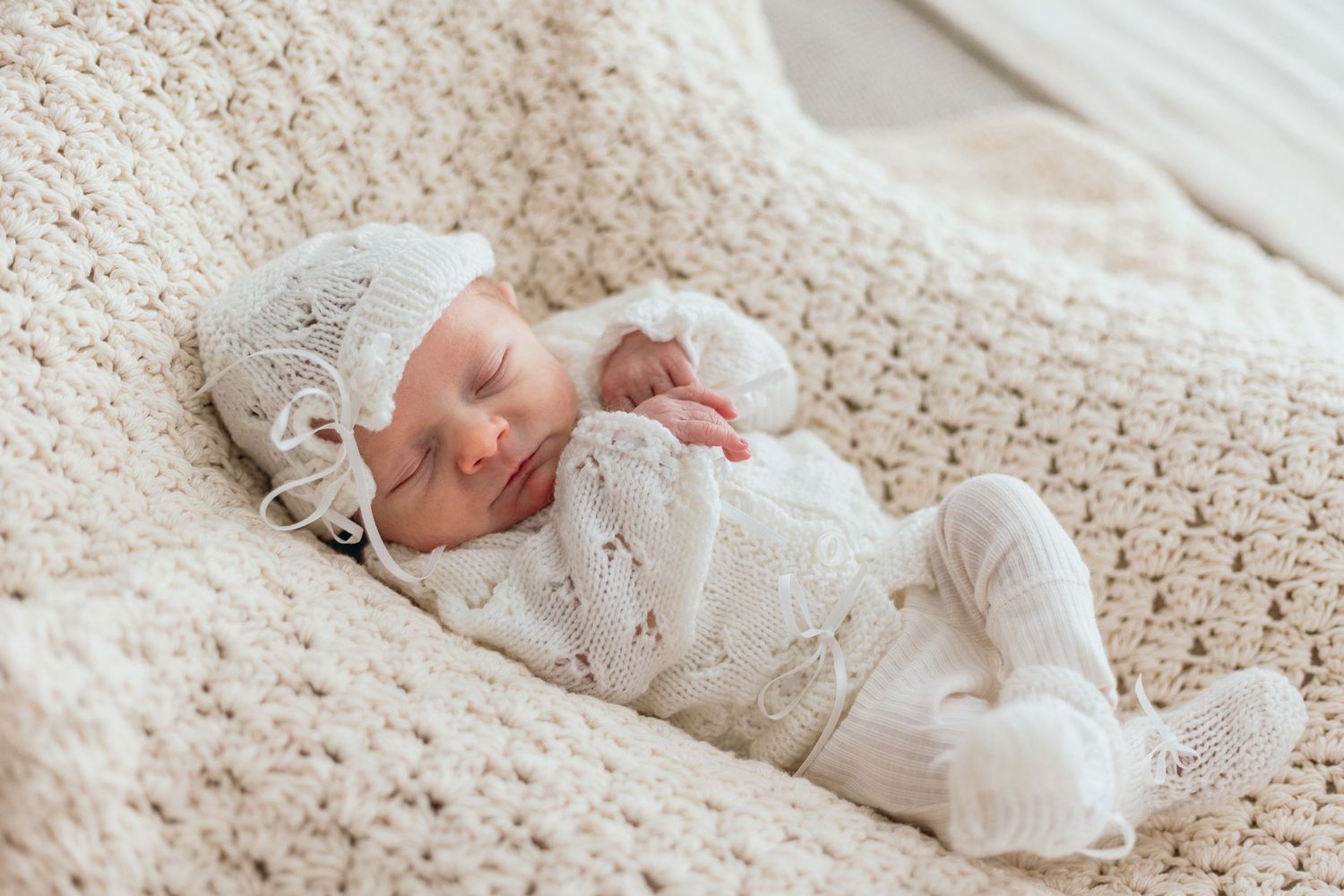 Newborn baby sleeping peacefully on cream knitted blanket.