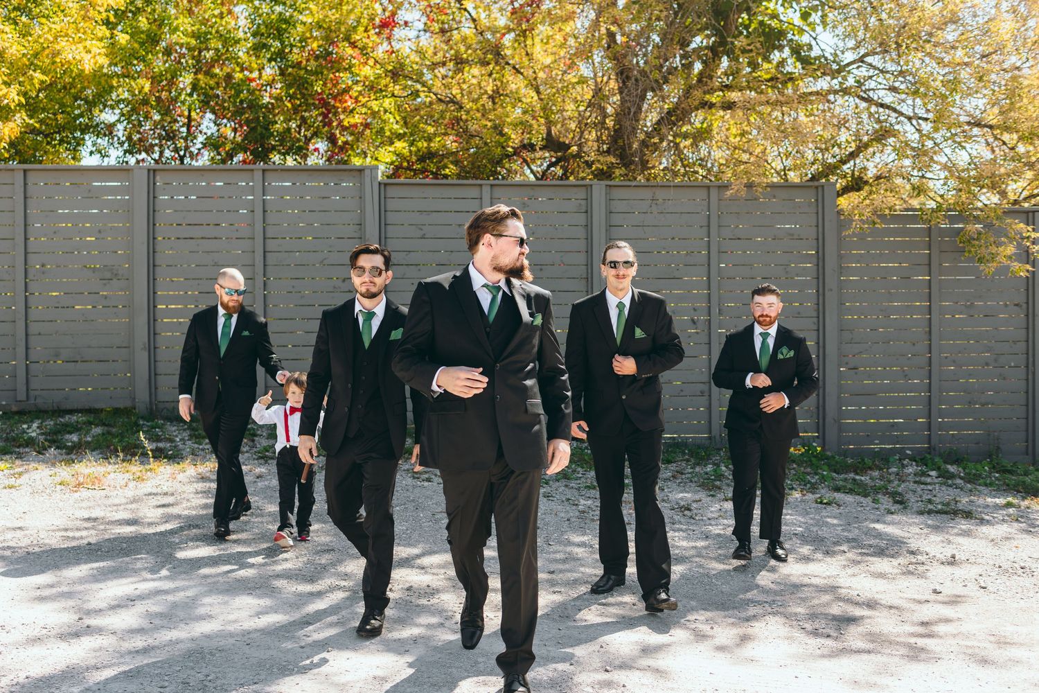 Wedding party walking and laughing together against a grey fence backdrop.