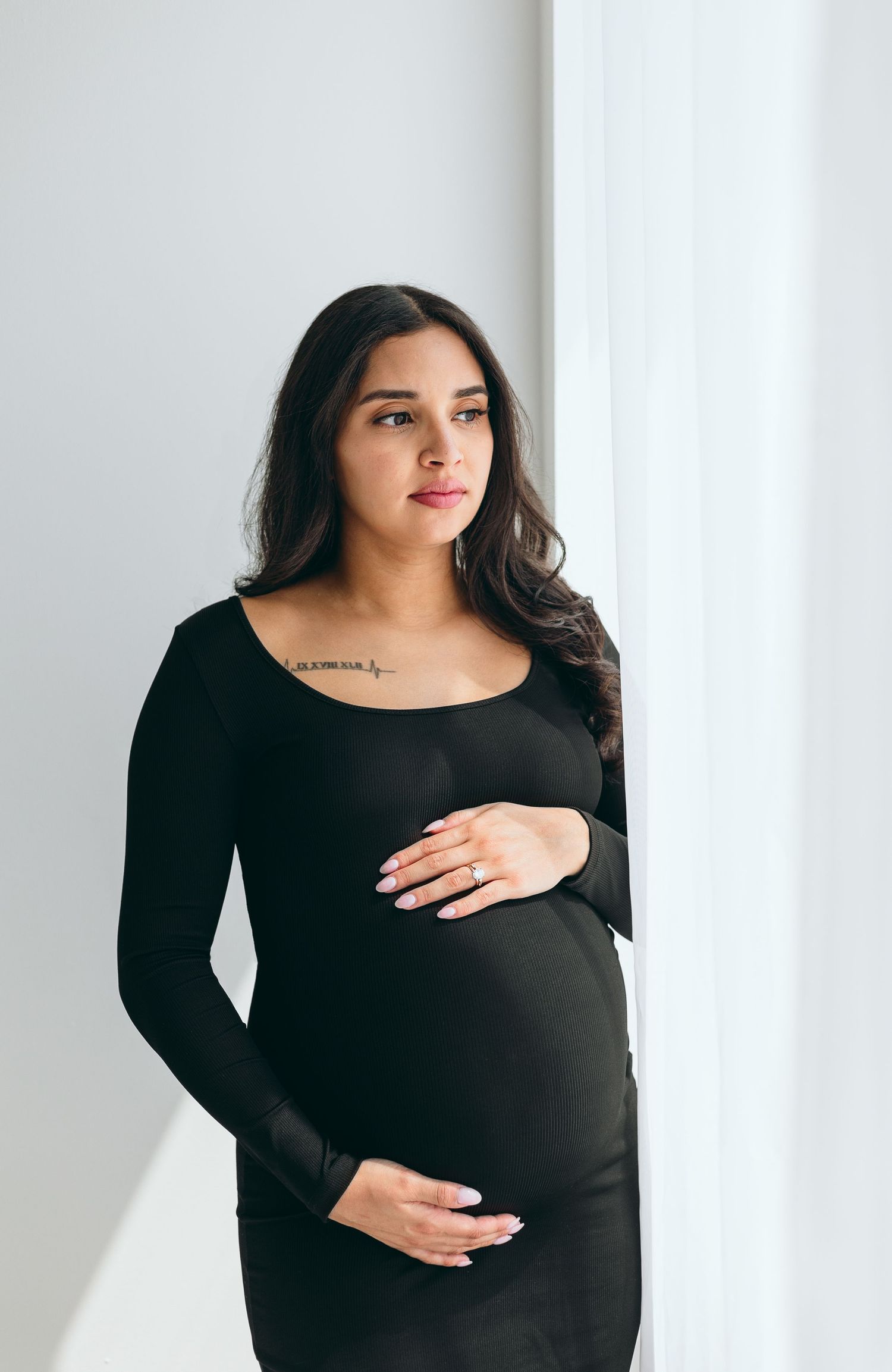 Woman in black dress cradling baby bump against white background.