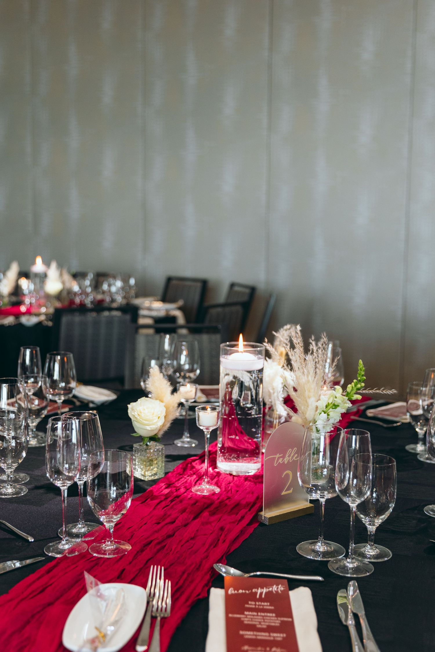 Wedding reception table set with black linens, red accents, and crystal wine glasses.