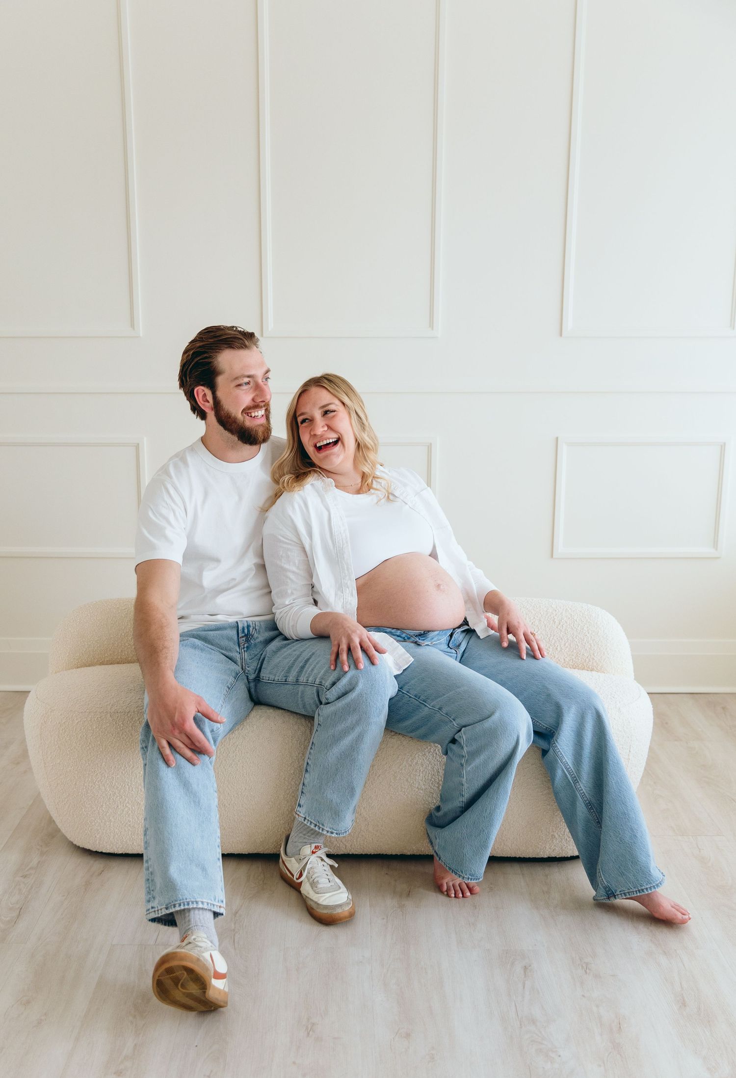 Couple sharing intimate laughs while relaxing on white couch in bright room.