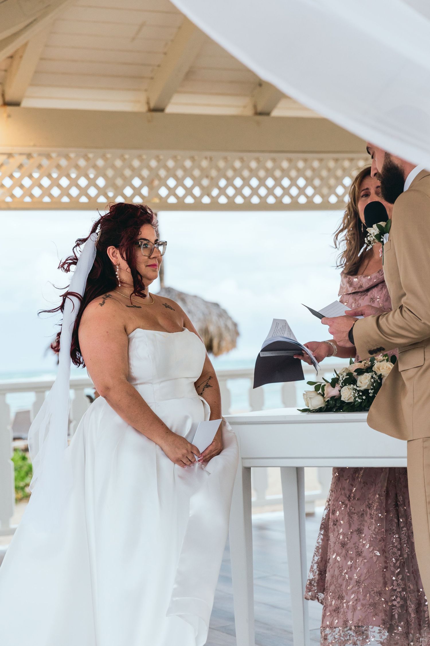 A wedding party celebrates in a white beachfront pavilion with lattice details.