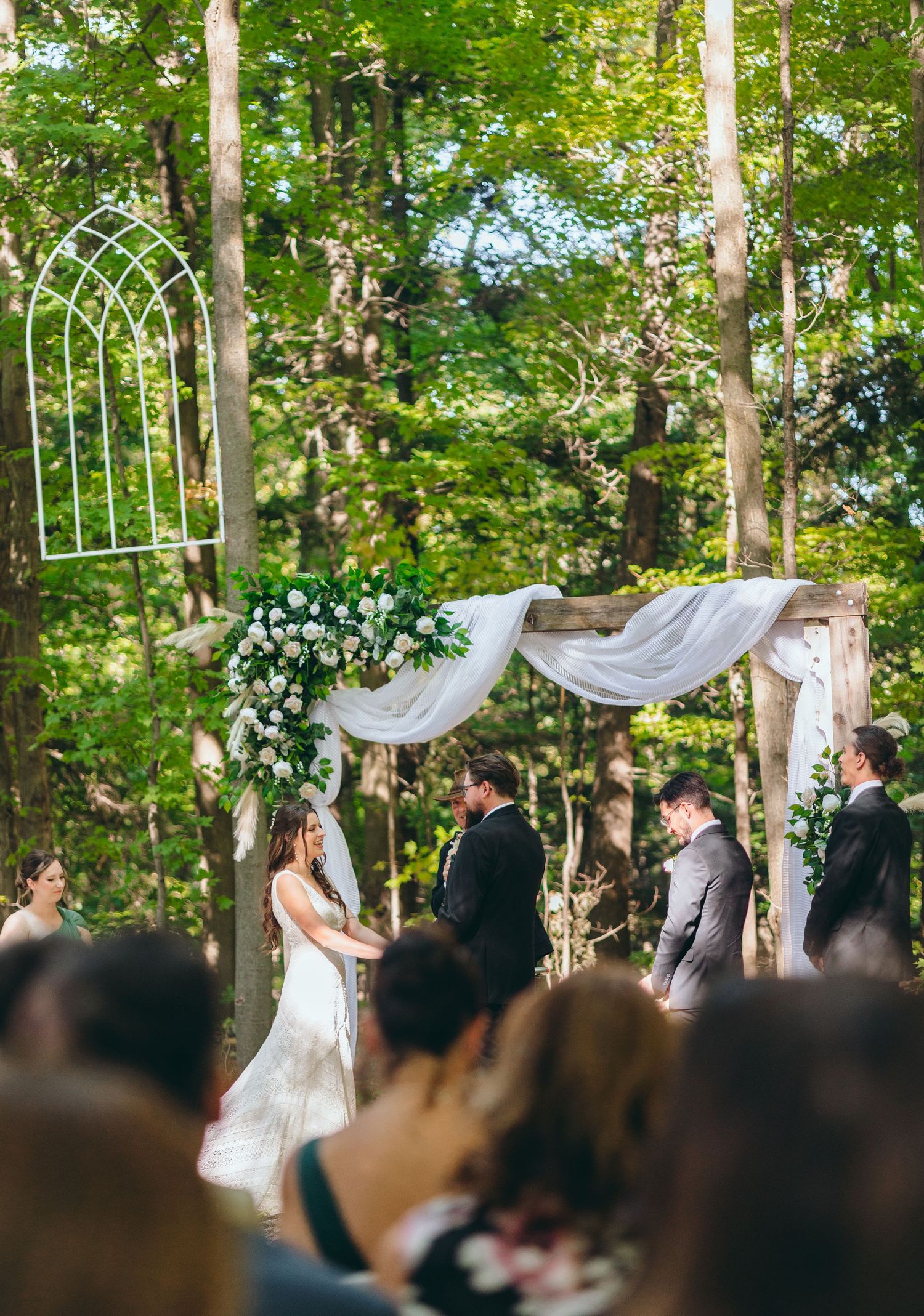 Outdoor forest wedding ceremony with white arch and floral decorations.