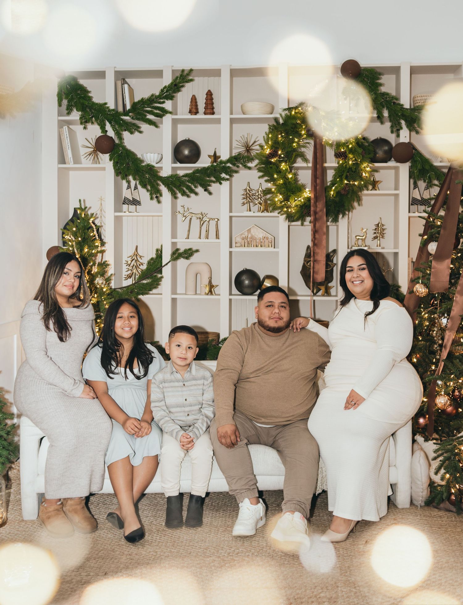Family of five posing together for a festive Christmas photo surrounded by holiday decorations and twinkling lights.