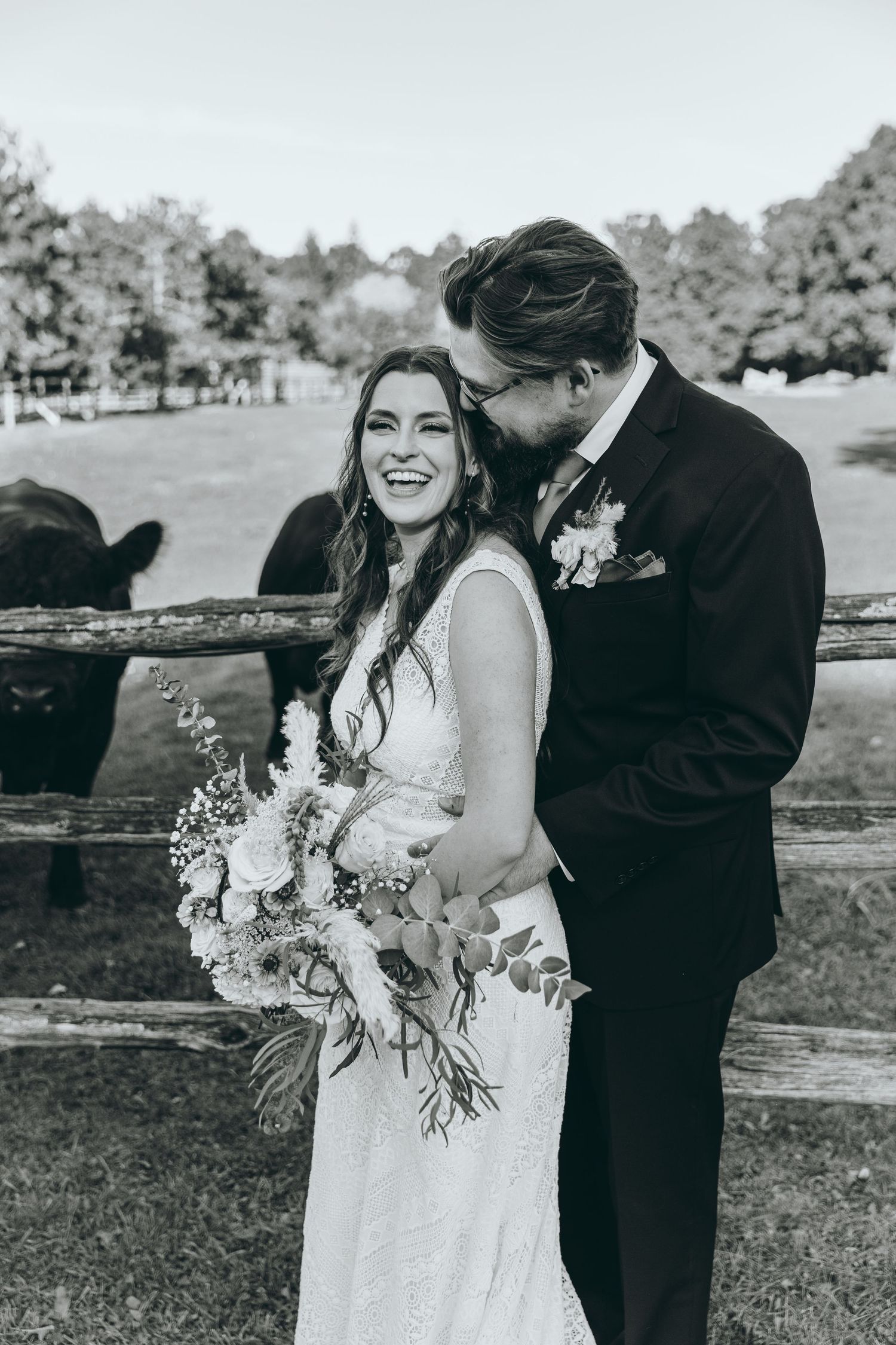 Black and white portrait of a tender moment by a rustic fence with bouquet.