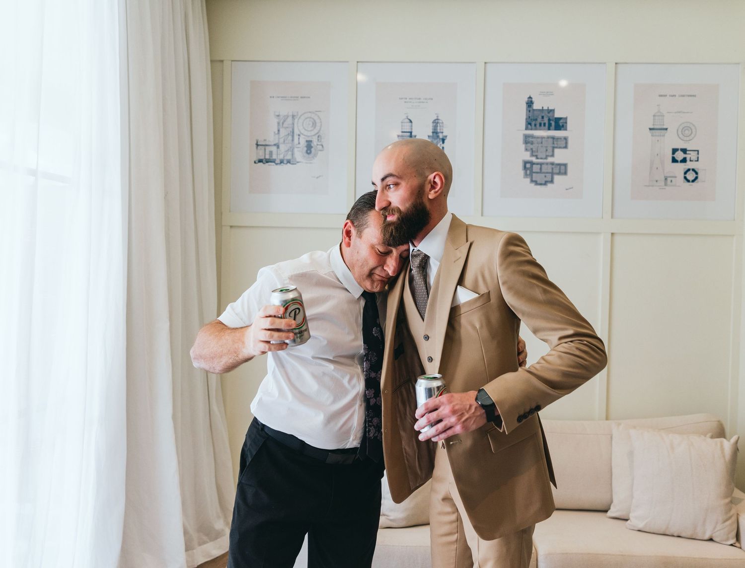 Person in tan suit holding a drink in an elegant room with framed artwork on walls.