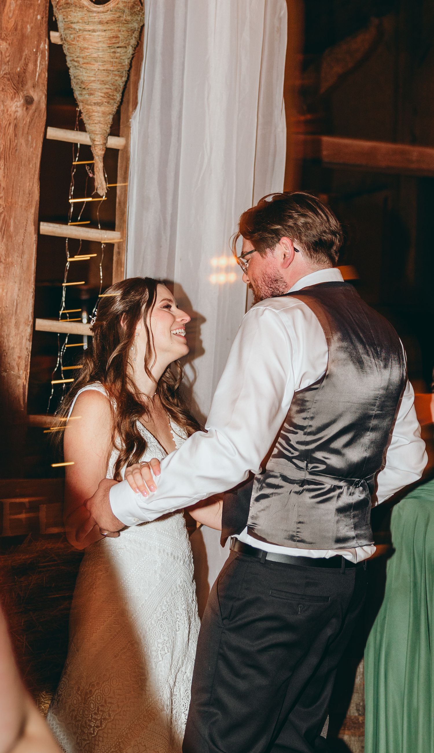 Couples dancing energetically at a wedding reception in a rustic venue with wooden beams and warm lighting.