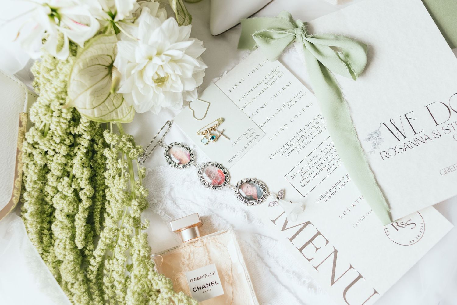 Wedding details flatlay with white flowers, rings, perfume and menu cards on light background.