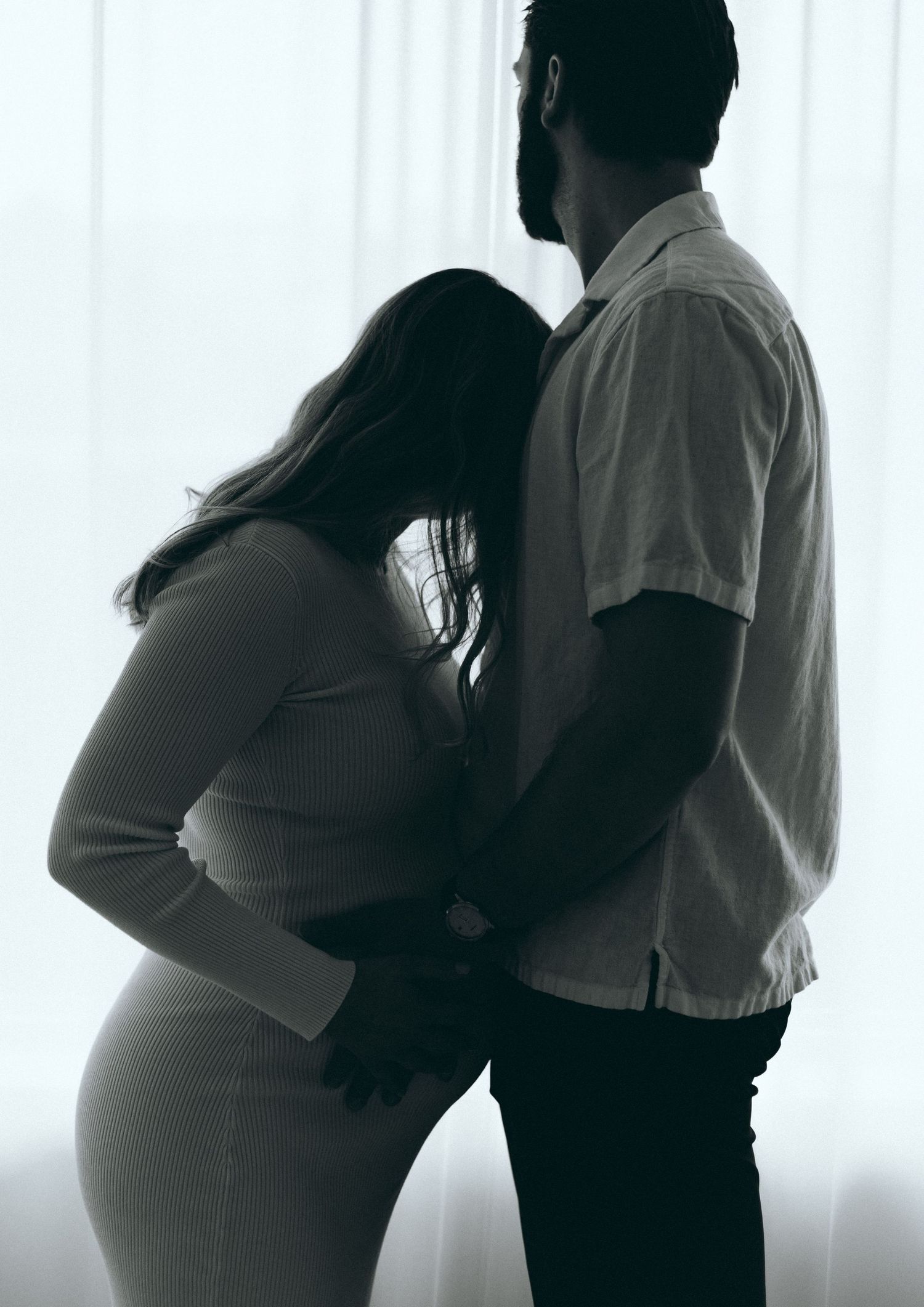 Silhouette series capturing intimate maternity moments against window light.