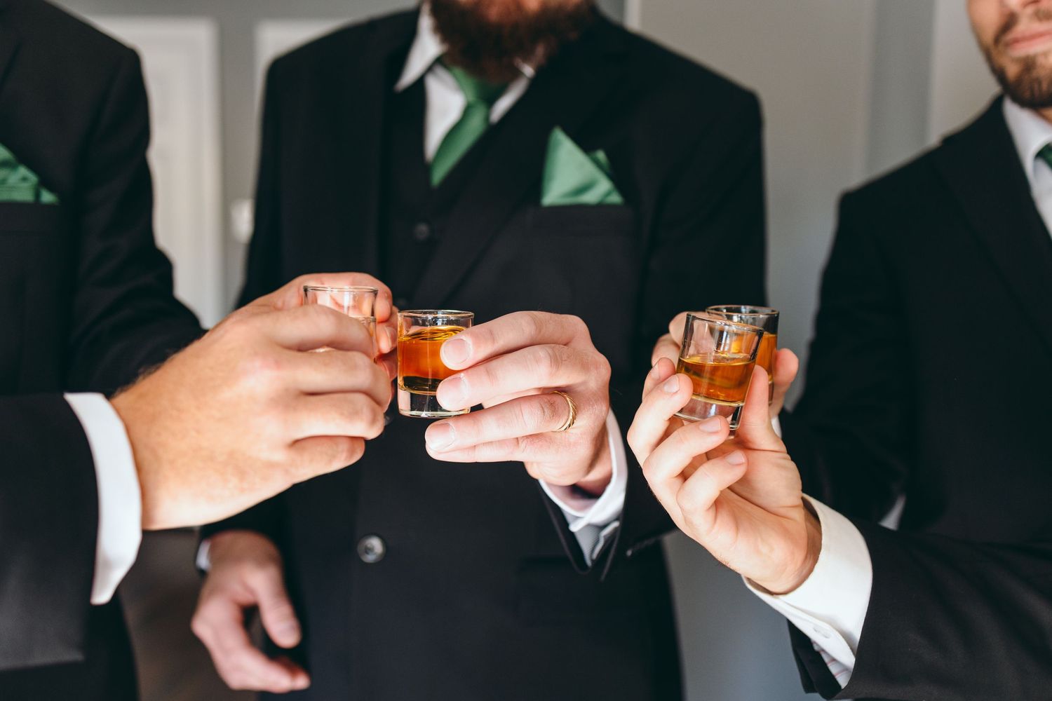 Men in formal black suits toasting with drinks during a wedding celebration.