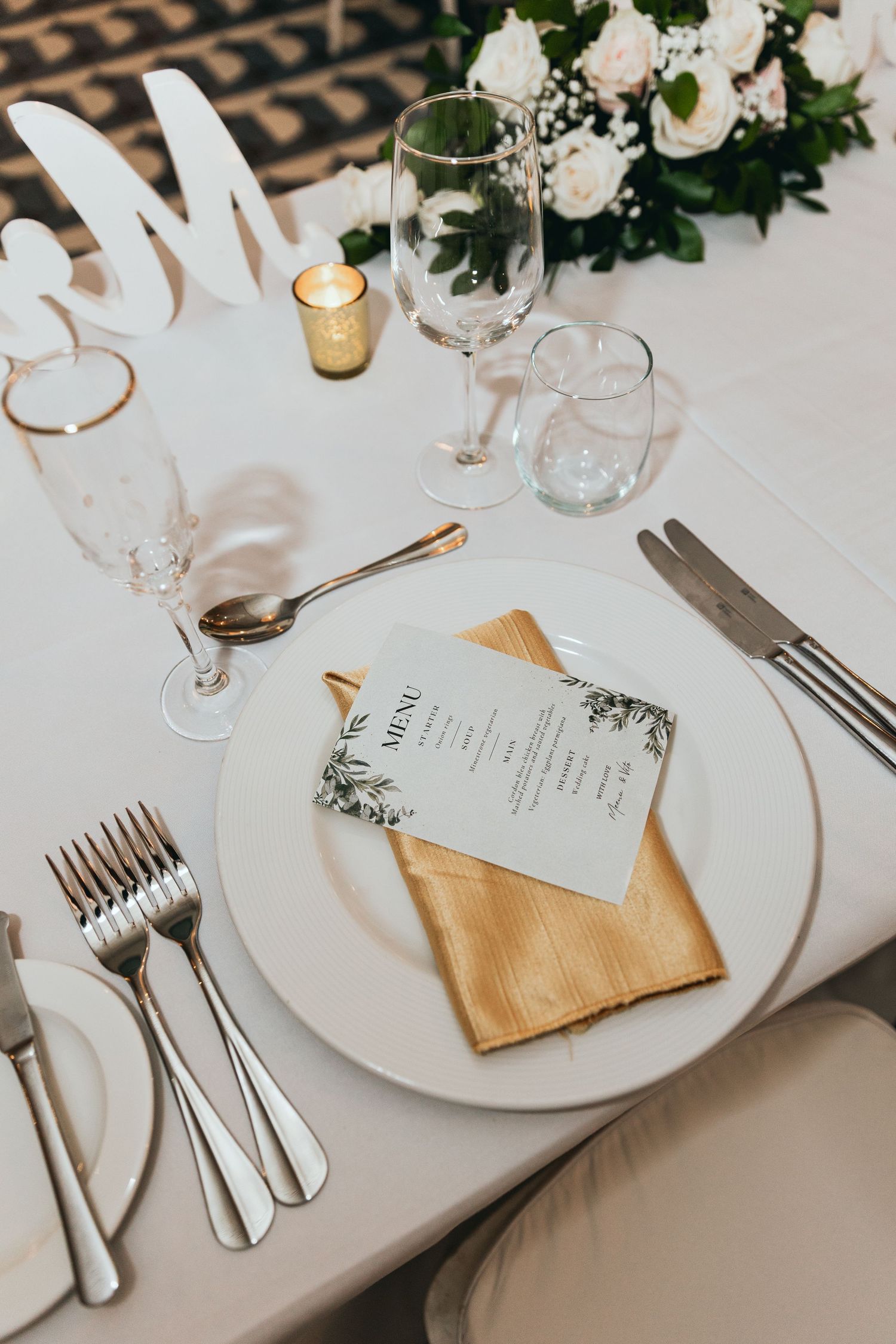 Formal place settings with gold napkins and white floral centerpieces at a wedding reception.