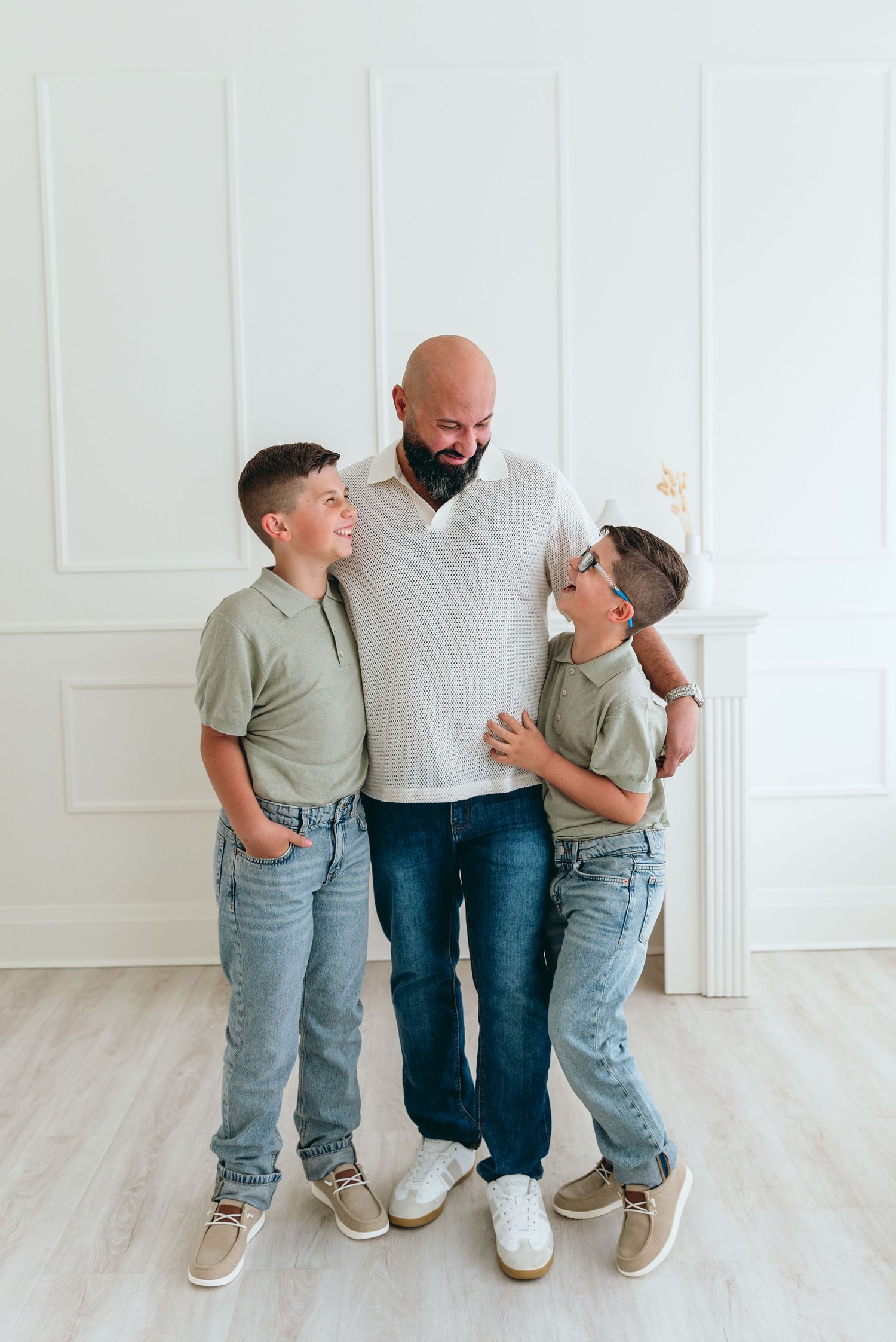 Family portrait with children in matching outfits sharing playful moment against white paneled wall.