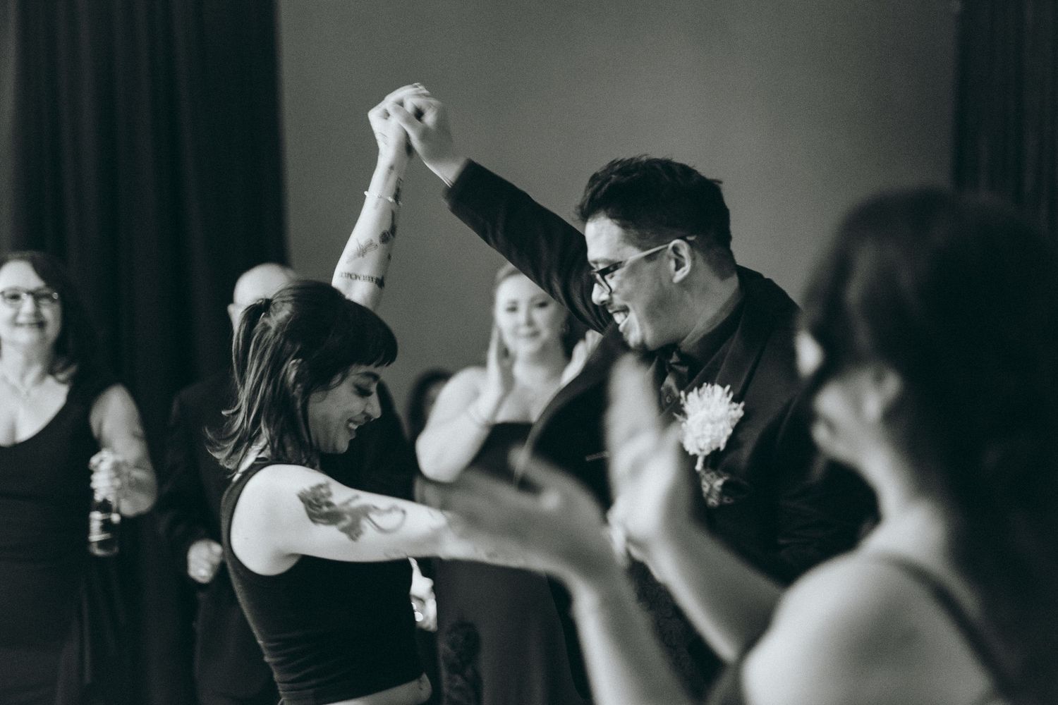 Wedding guests dancing and celebrating at a reception with dramatic black and white lighting.