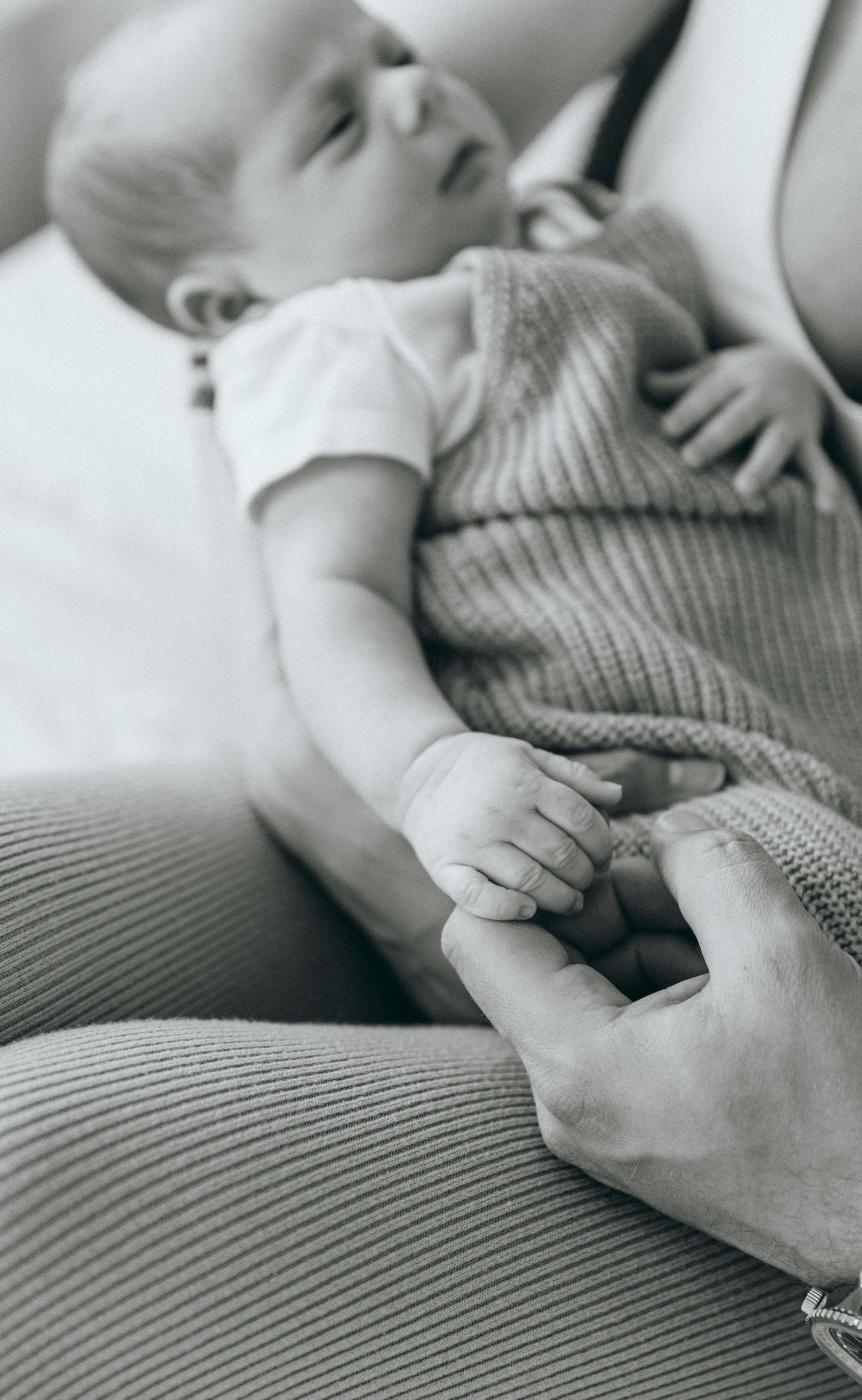 Black and white image of a sleeping baby's hand being held while wearing knit clothing.