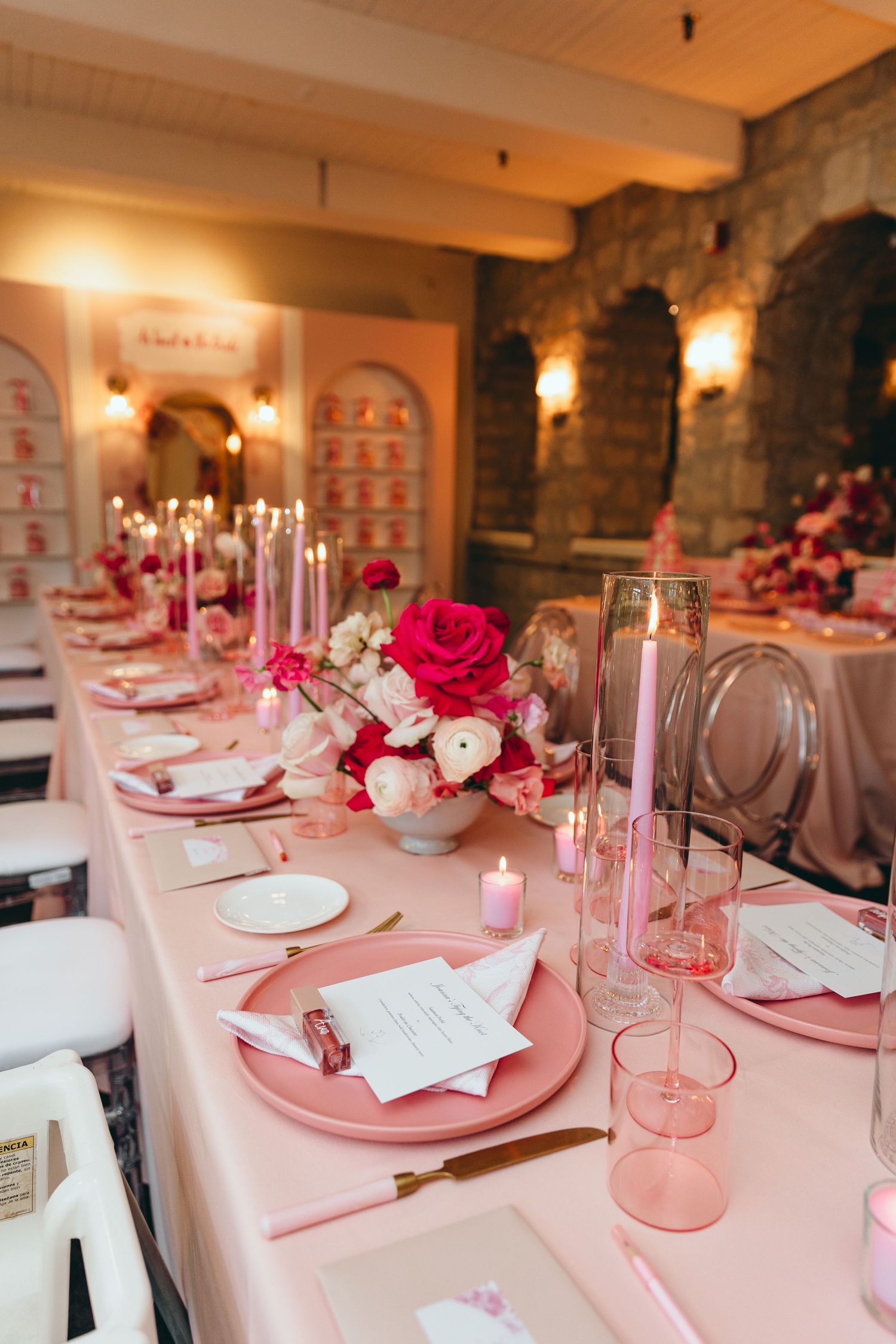 Romantic table setting with pink placemats, roses, and candlelight in rustic venue.