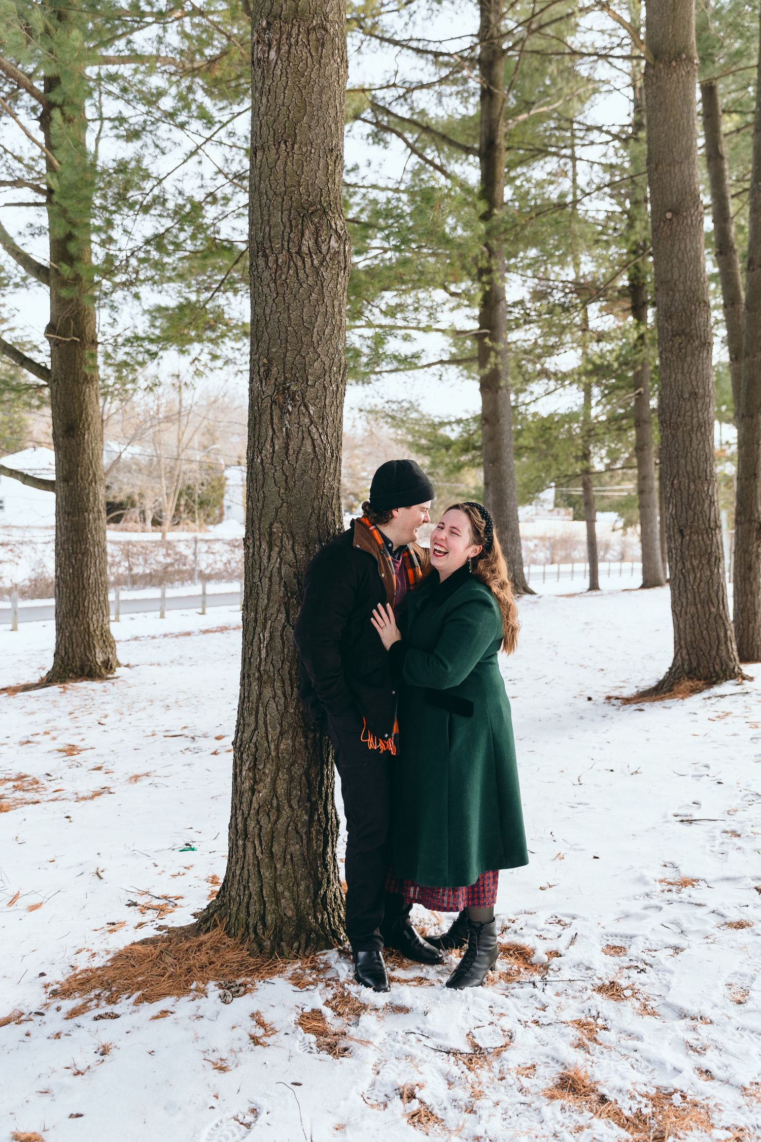 Playful winter engagement photos among snow-covered pine trees.
