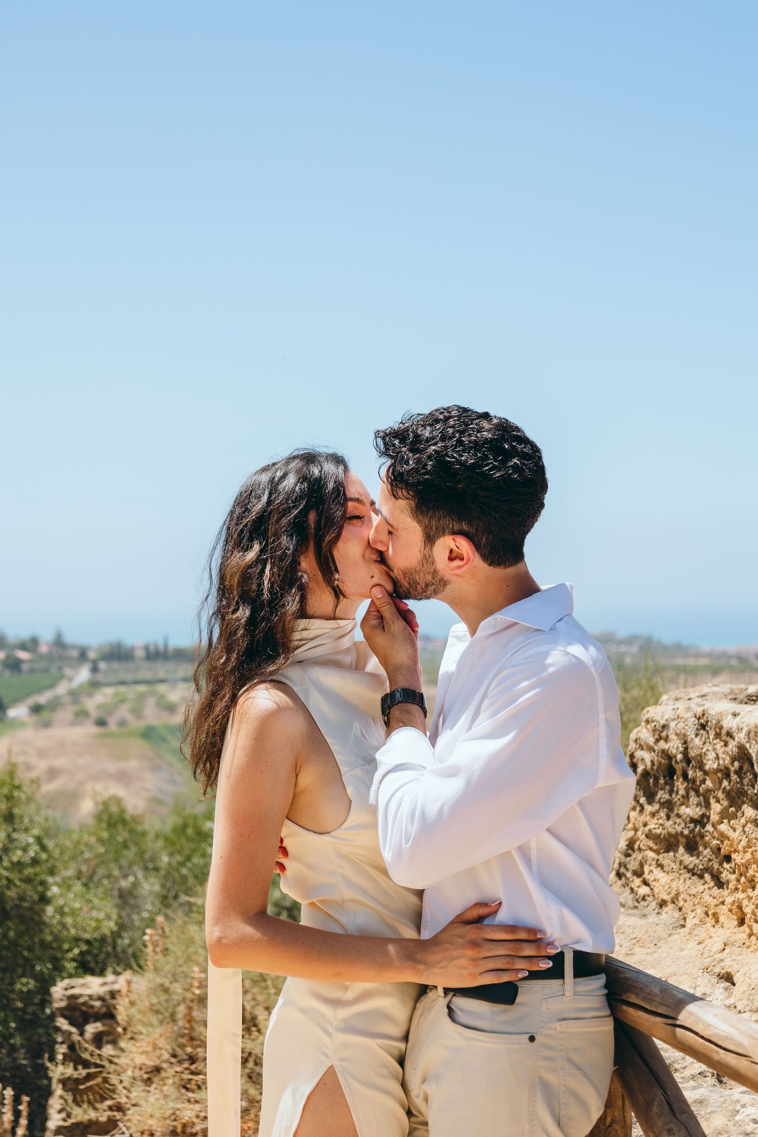 A romantic moment captured against a scenic coastal backdrop with blue skies.