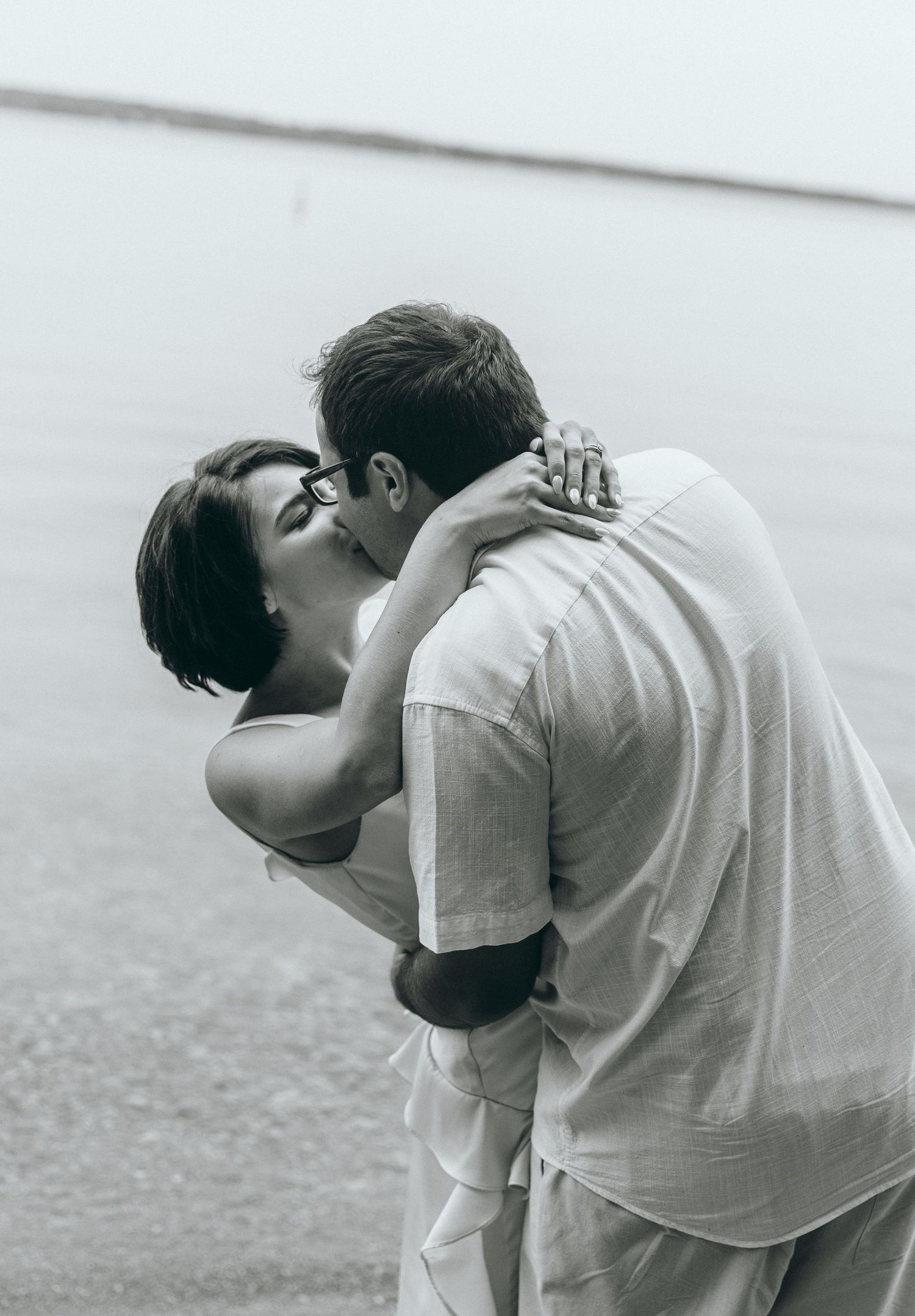 An intimate black and white photo of a couple embracing by the water.