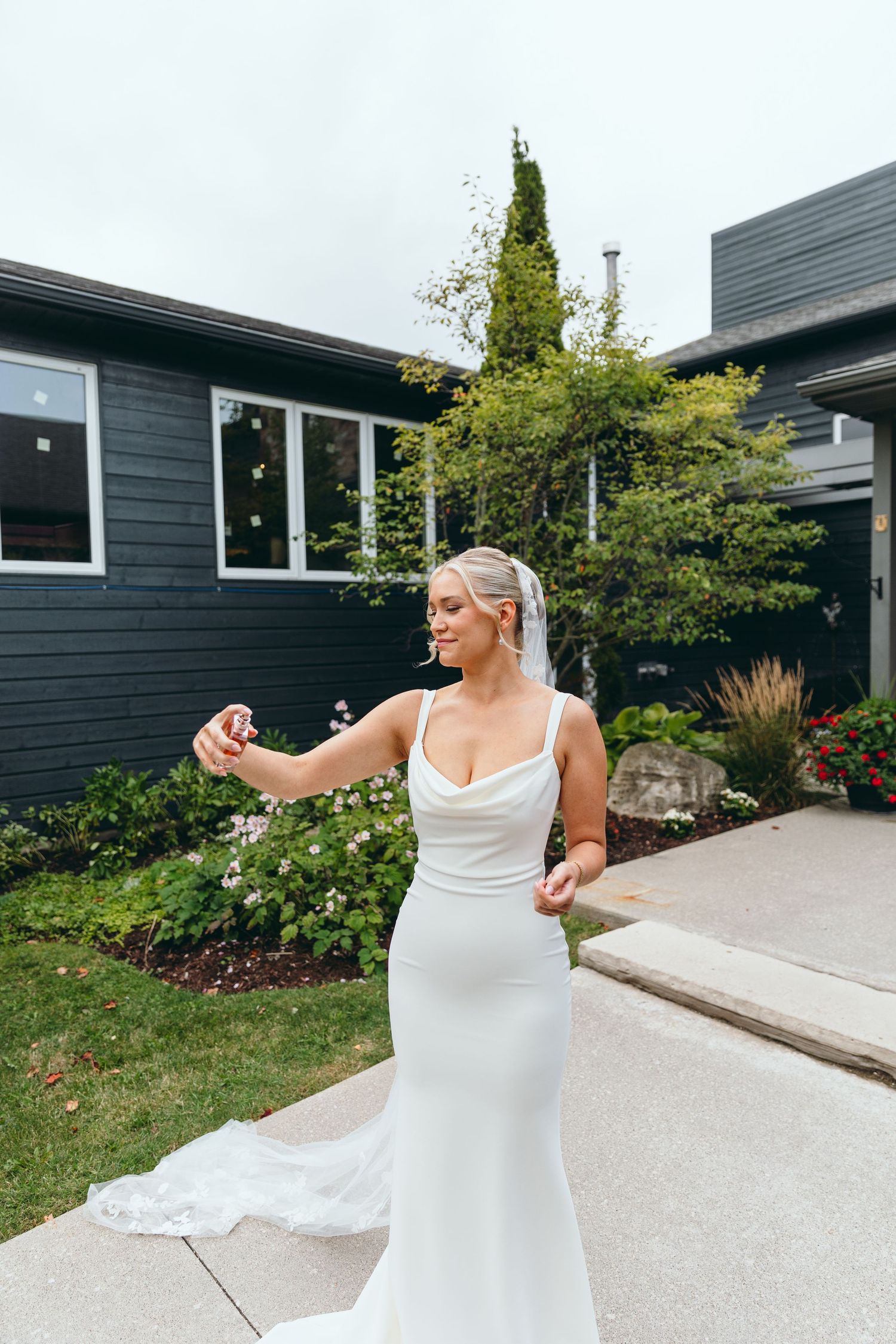 Bride in white dress twirling on concrete path near modern building with landscaping.