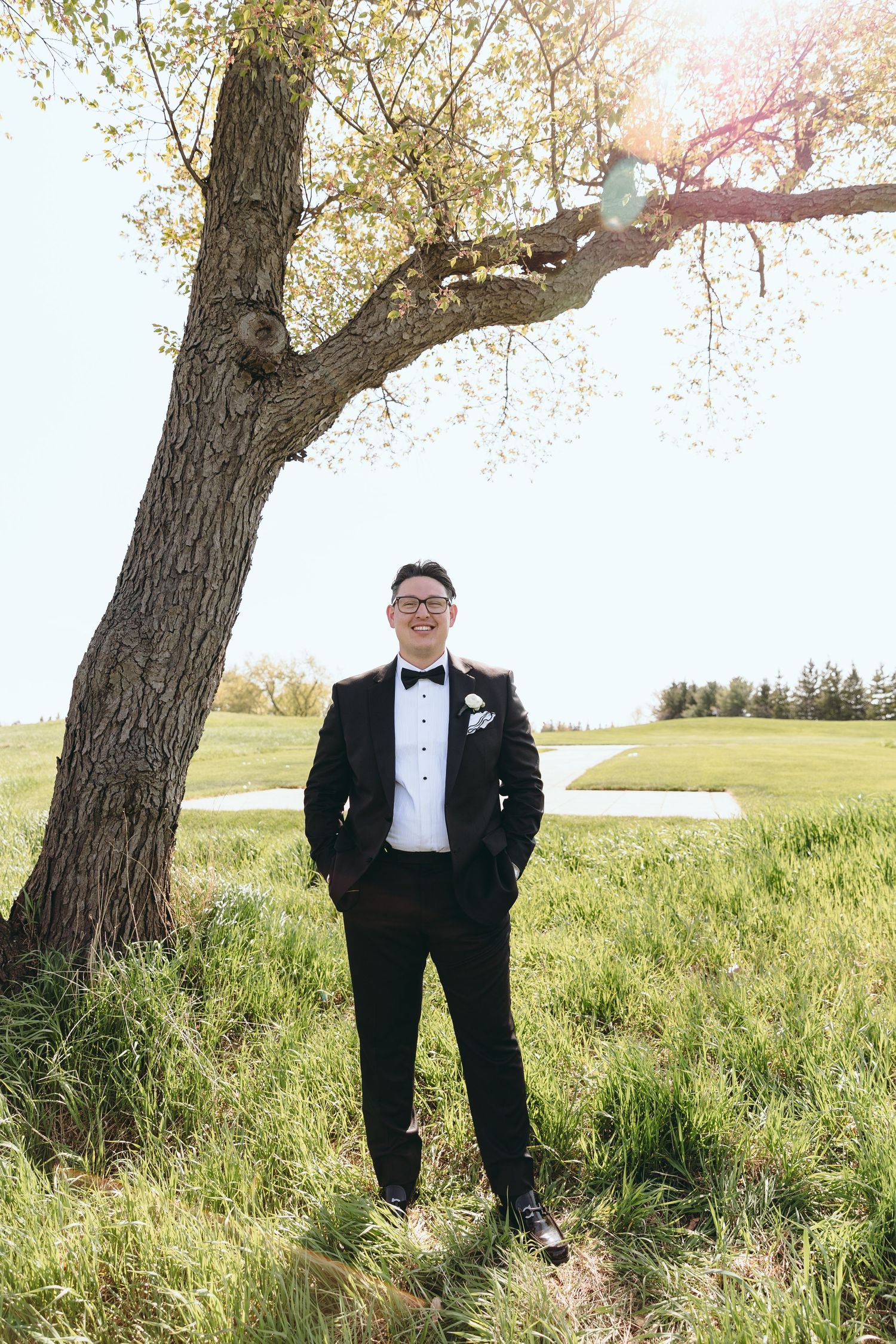 Formal portrait of groom standing under a large tree on a golf course.