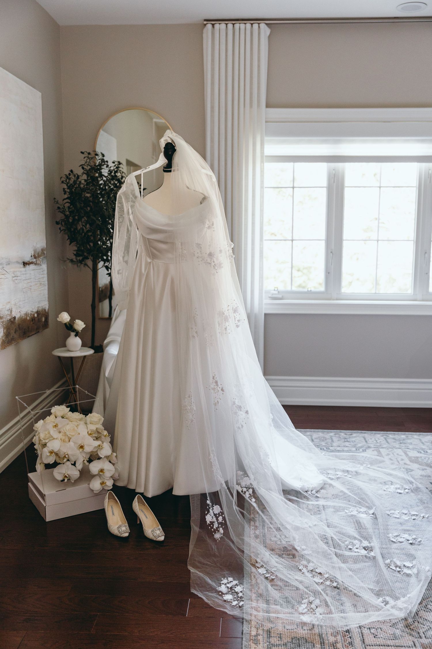 Elegant white wedding dress with lace train displayed in a bright room with hardwood floors.