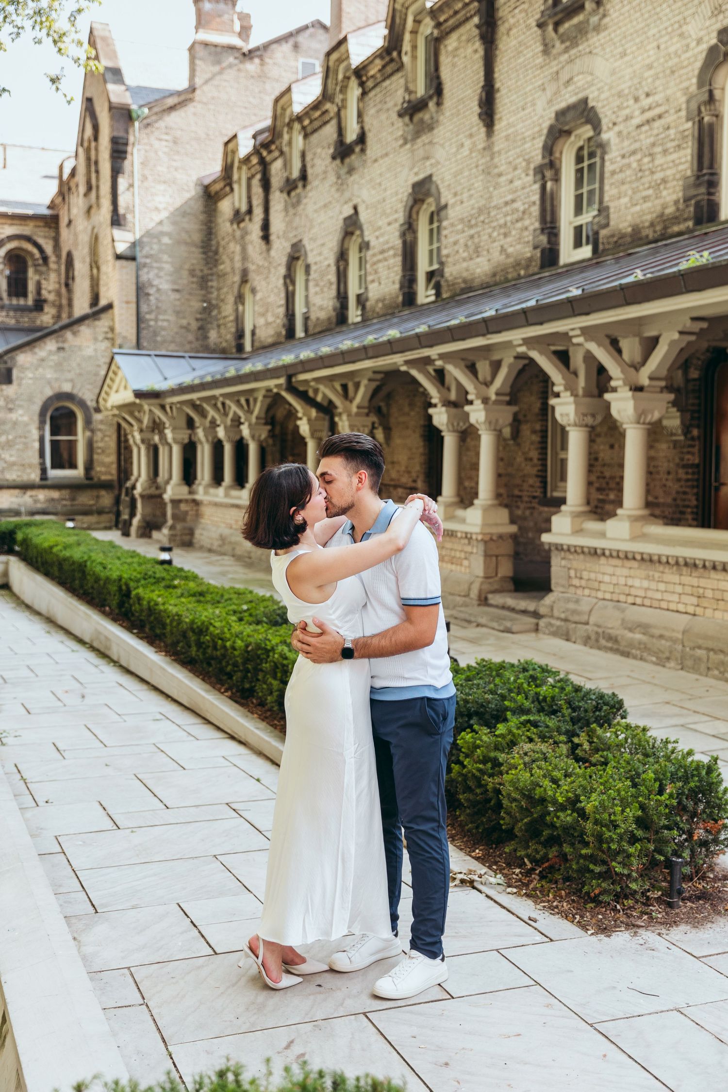 A couple embraces in front of a historic building with Gothic columns.