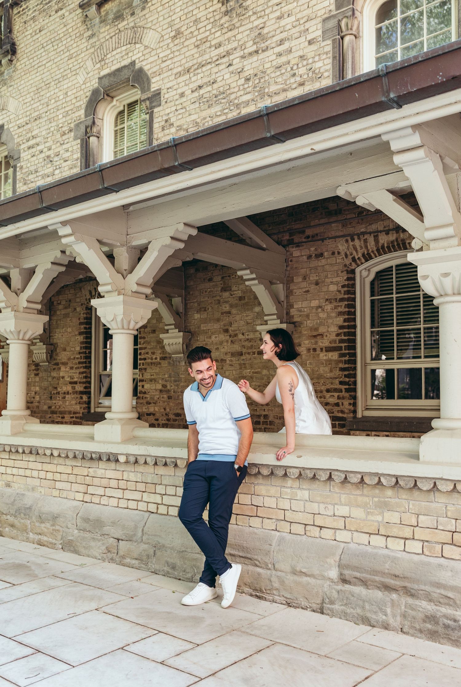 A couple shares a playful moment along a historic stone colonnade with decorative pillars.