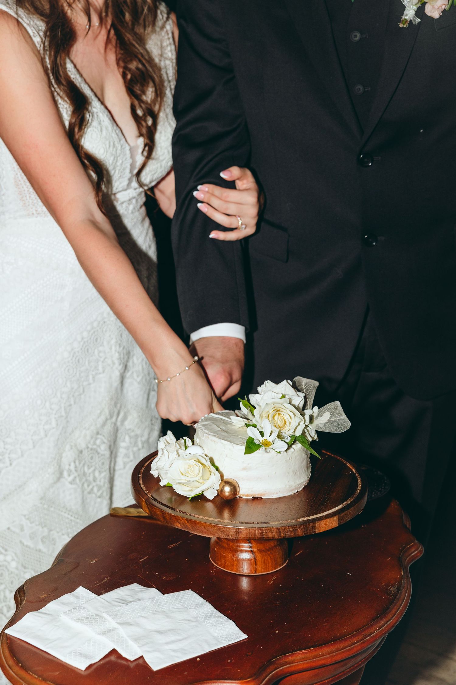Close-up of couple cutting their white wedding cake on wooden table.