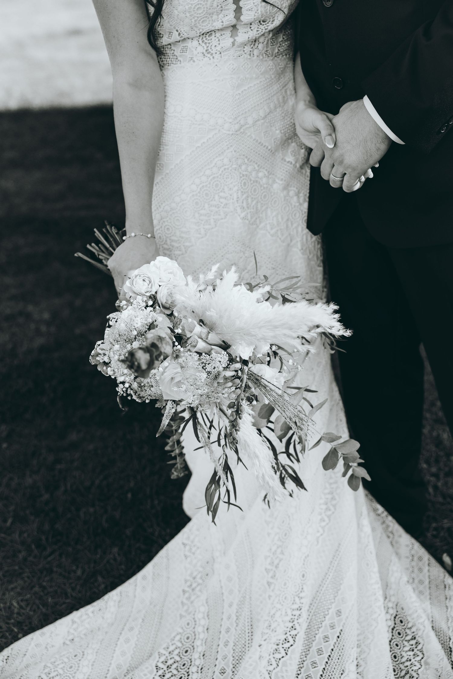 Close-up detail of a lace wedding dress and white floral bouquet with greenery.