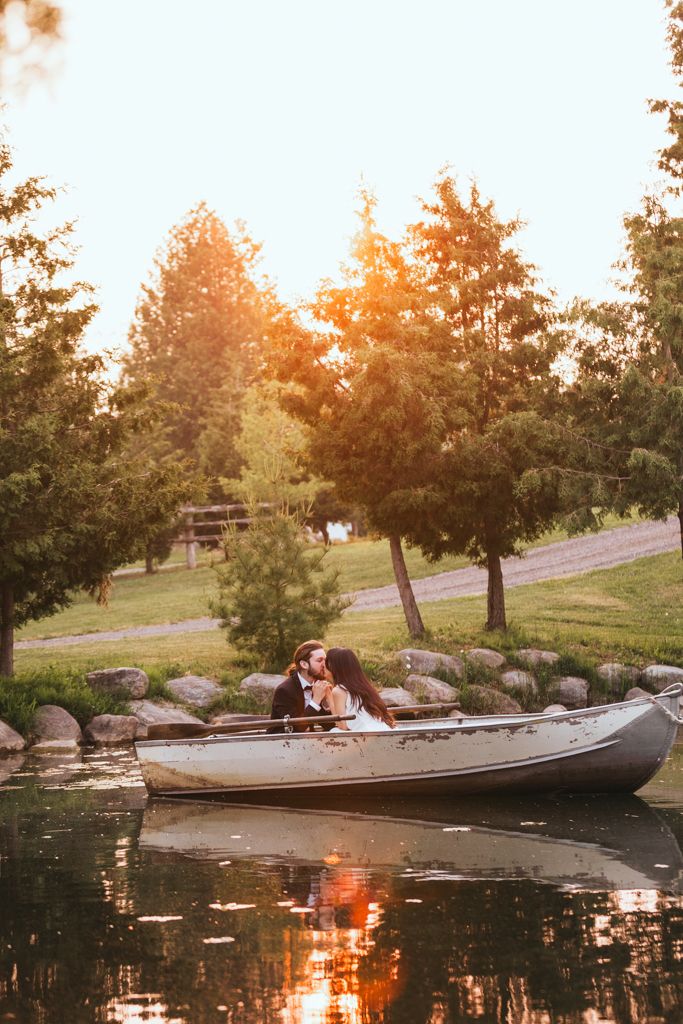 Newlyweds share a romantic moment in a canoe during golden hour by a tree-lined shore.