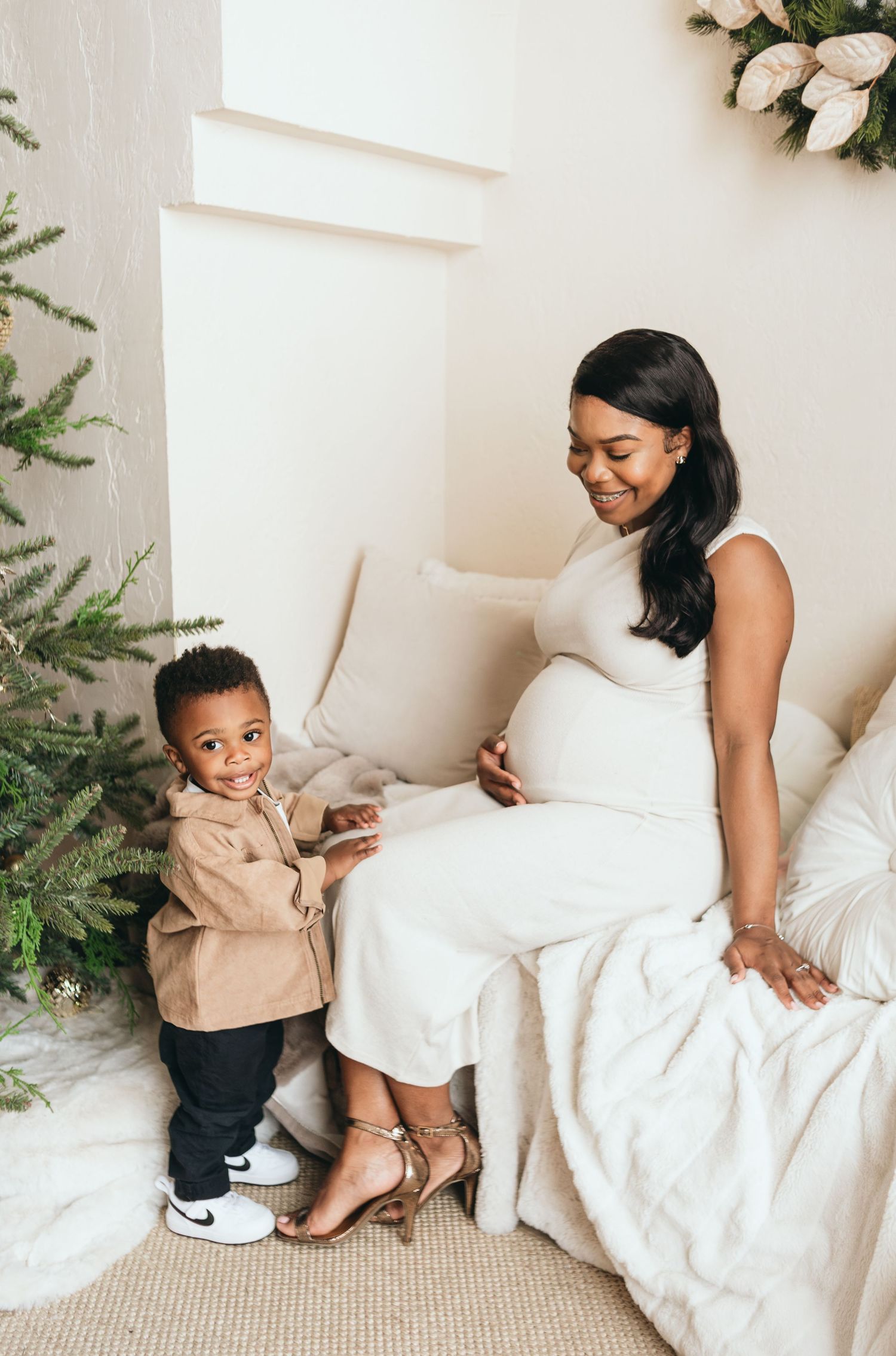 A heartwarming maternity photo featuring a white dress and festive holiday decor with a Christmas tree.