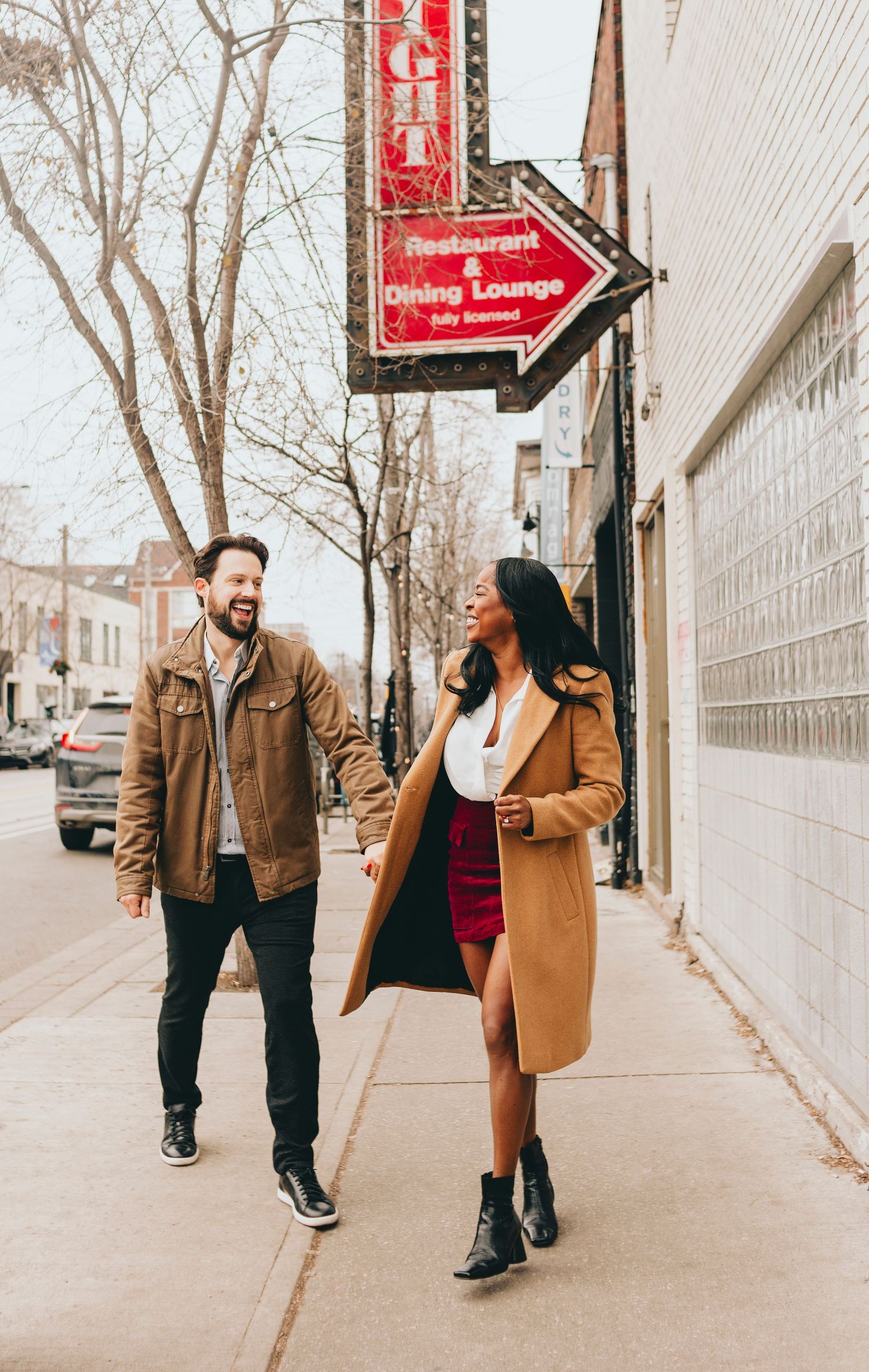 Casual couple strolling past red dining lounge sign on city street.