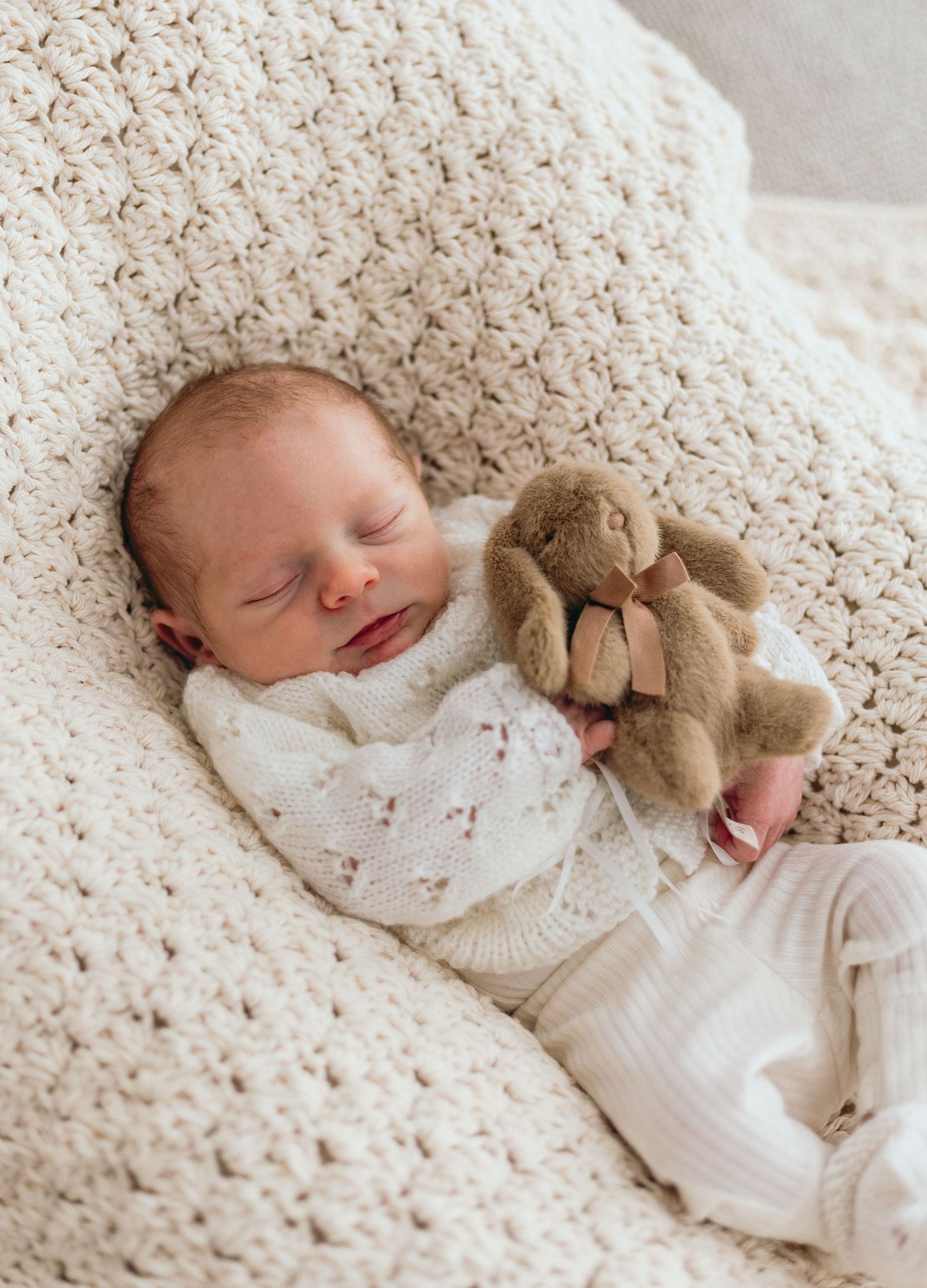 Sleeping newborn with teddy bear on crocheted cream blanket.