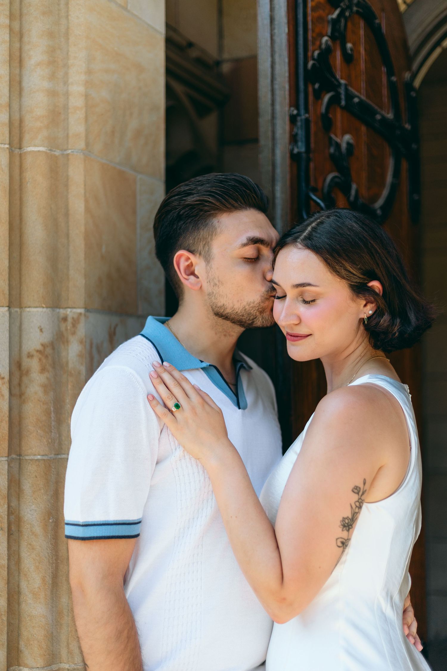 Romantic embrace shared between couple in matching white attire by stone architecture.