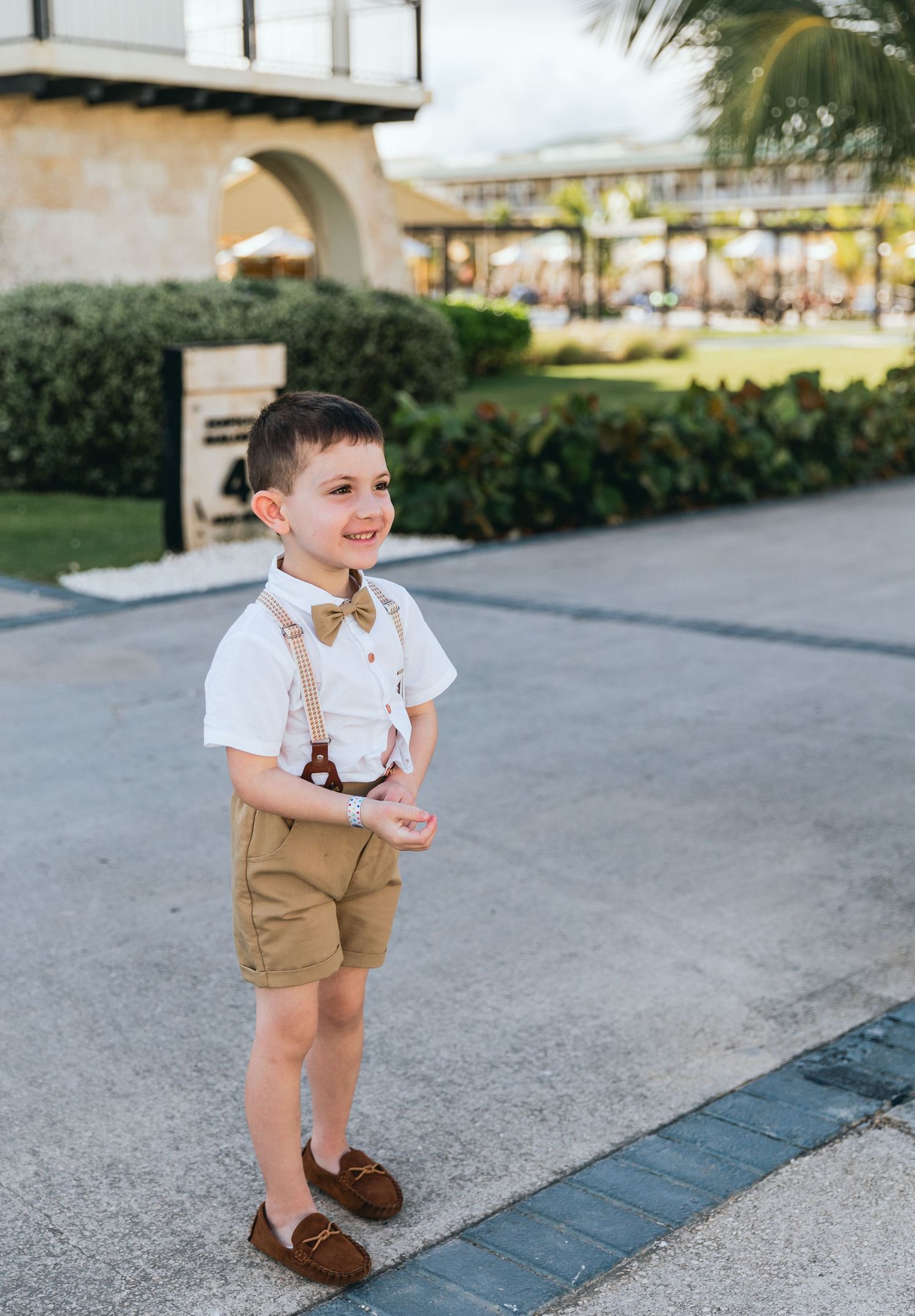 Young boy in formal attire smiles while walking during wedding celebration.