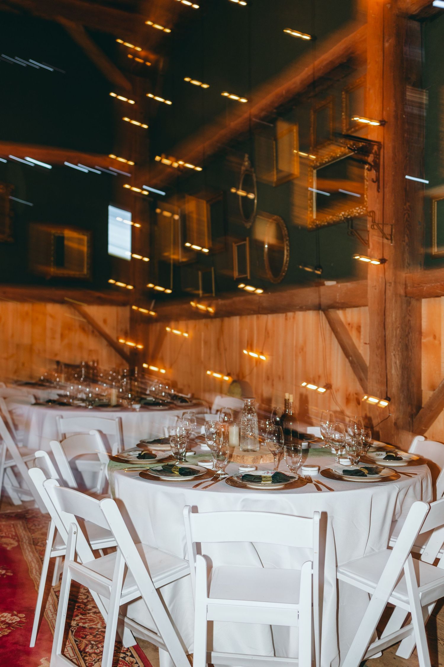 Wedding reception setup with white folding chairs and tables in rustic barn setting.
