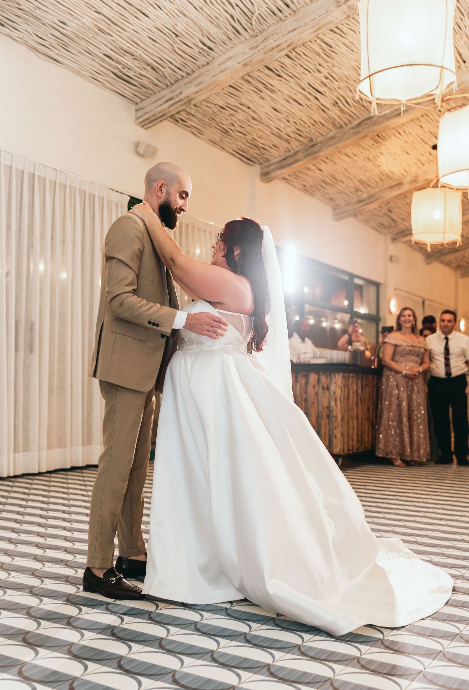 Couple performs romantic dip during their wedding dance on black and white patterned floor.