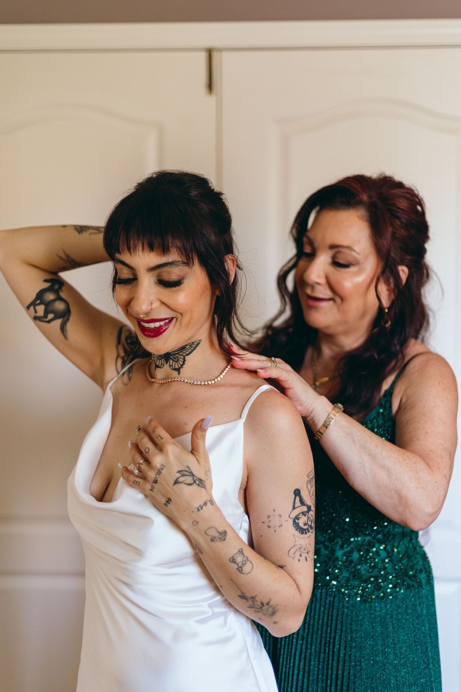 Two people in white and emerald green dresses sharing intimate moments during wedding preparations.
