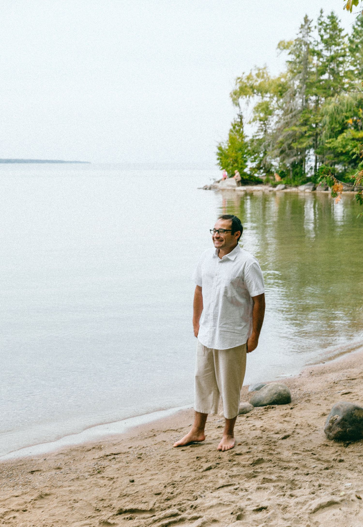 Person in white clothing walking along peaceful lakeside beach.