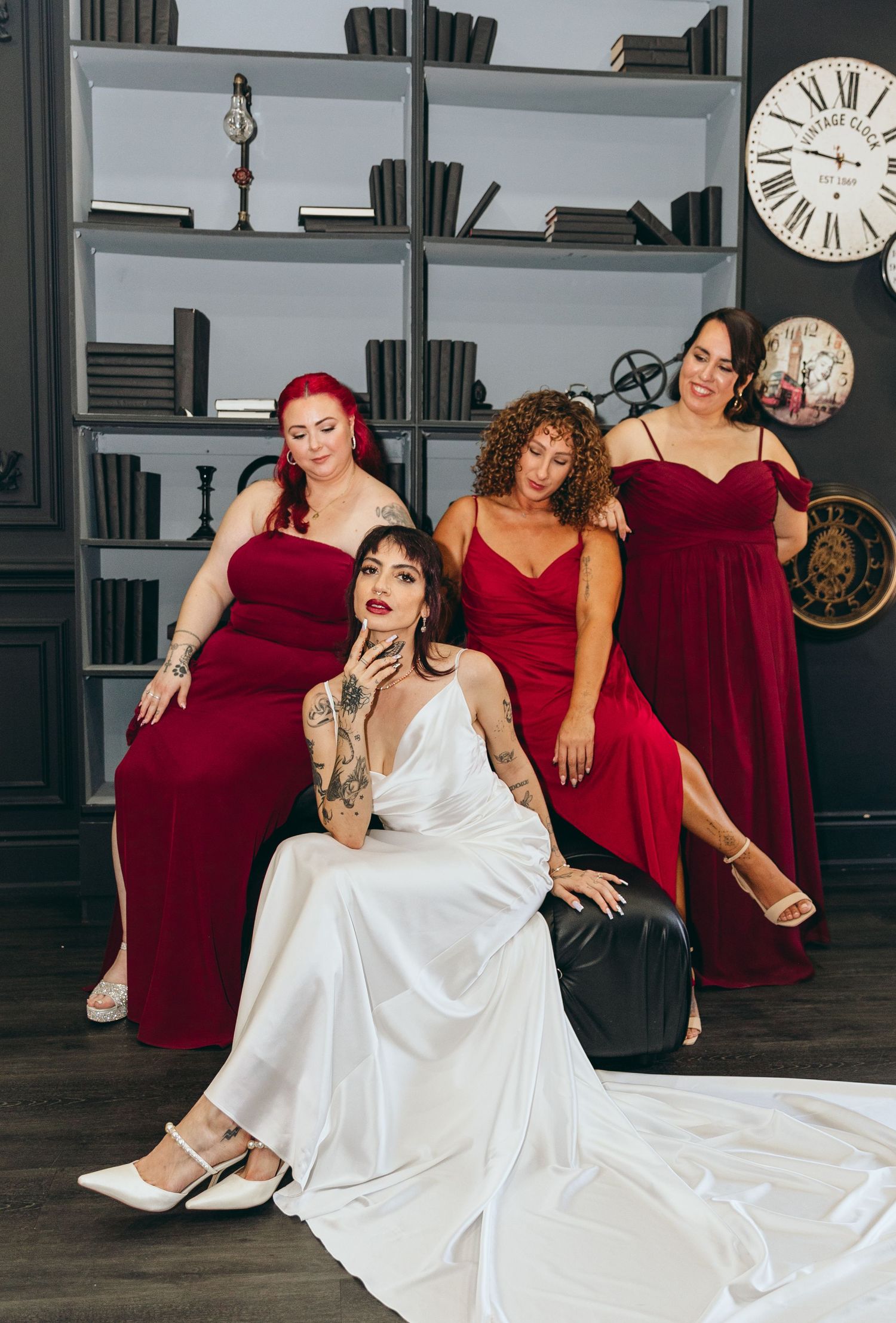 Wedding party in burgundy dresses lounge dramatically on floor during photo session.