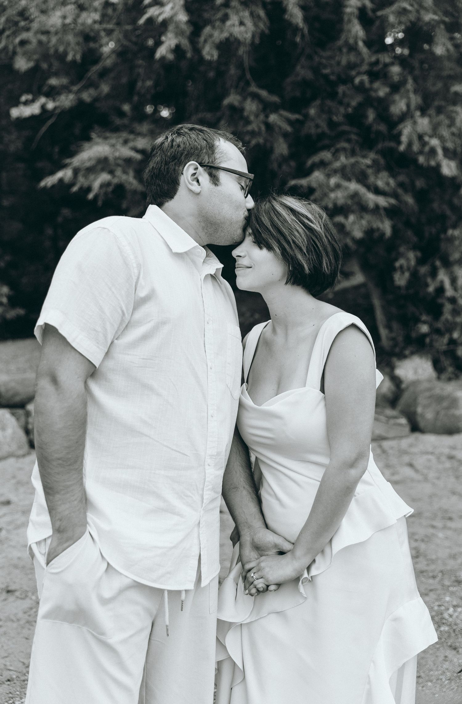 An intimate black and white portrait of two people in white clothing sharing a tender moment.