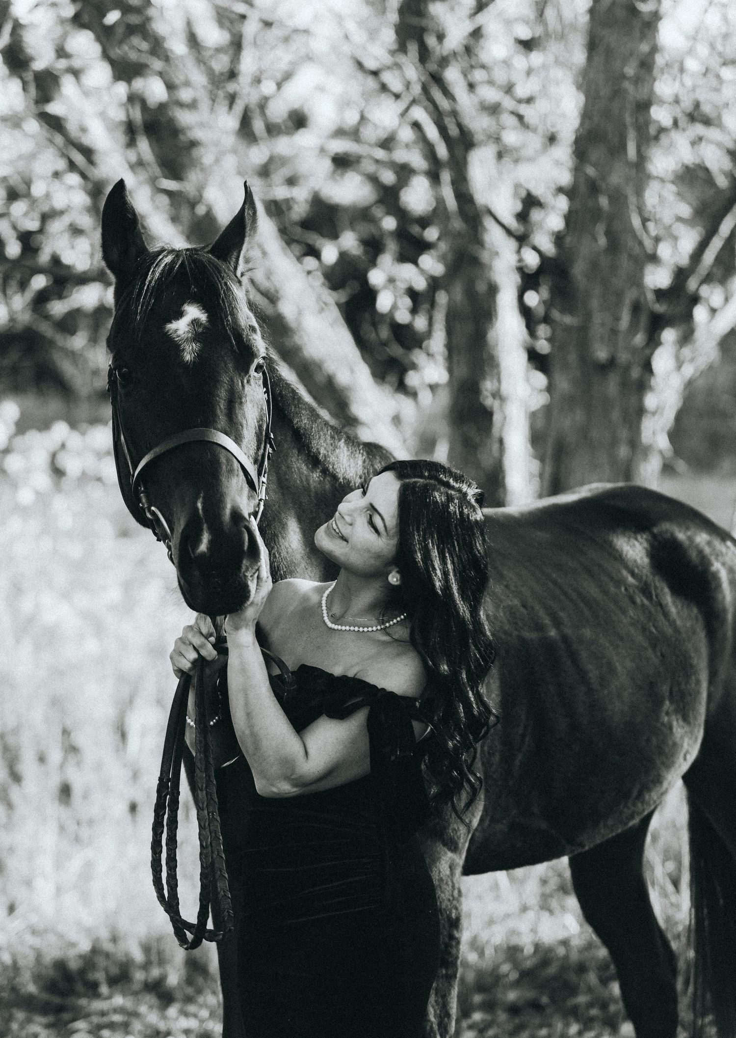 Black horse and handler in wooded setting captured in black and white.