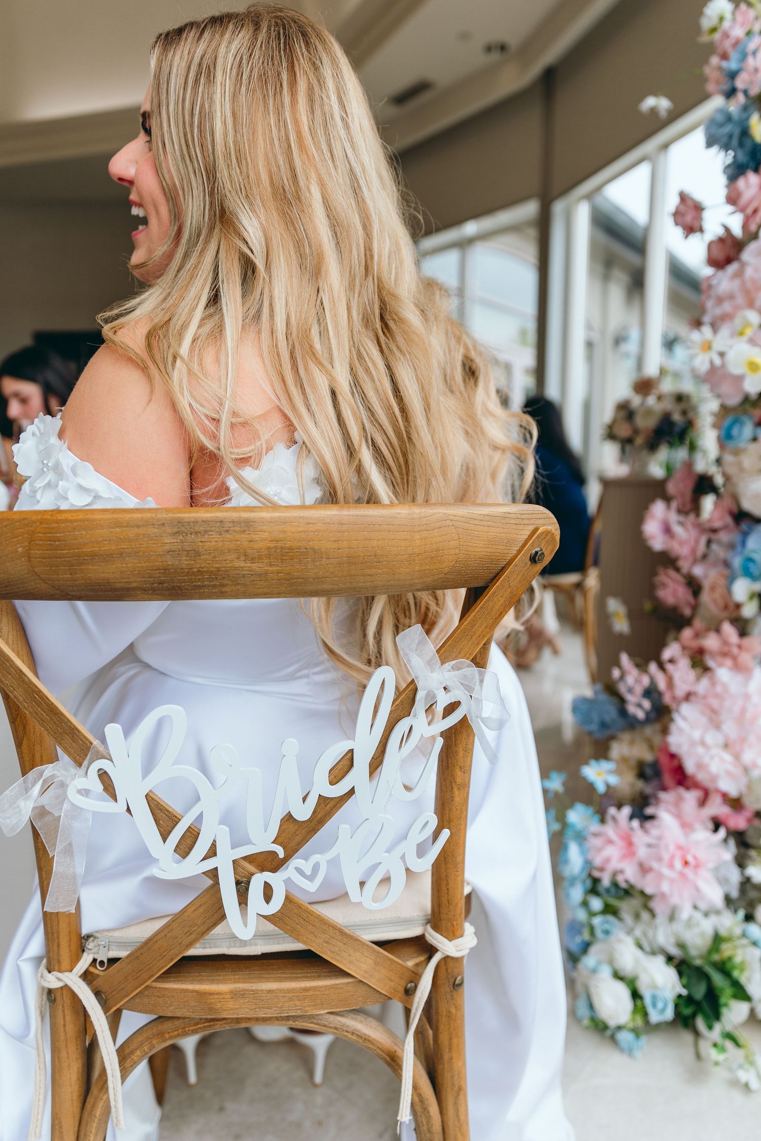 Wooden chairs decorated with white signage and floral arrangements at an elegant wedding reception.