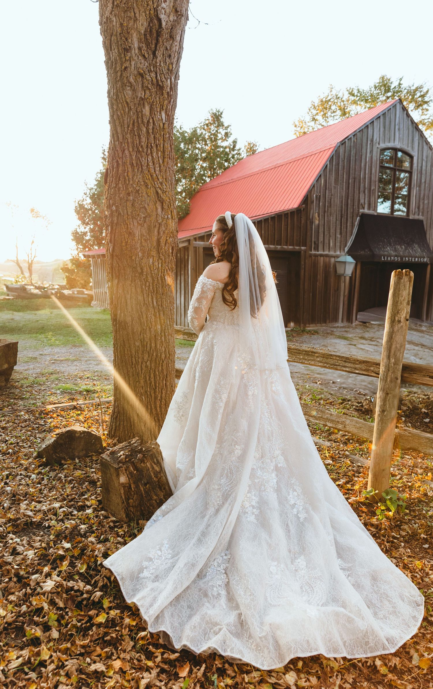 A flowing lace wedding dress photographed against rustic barns during golden hour.