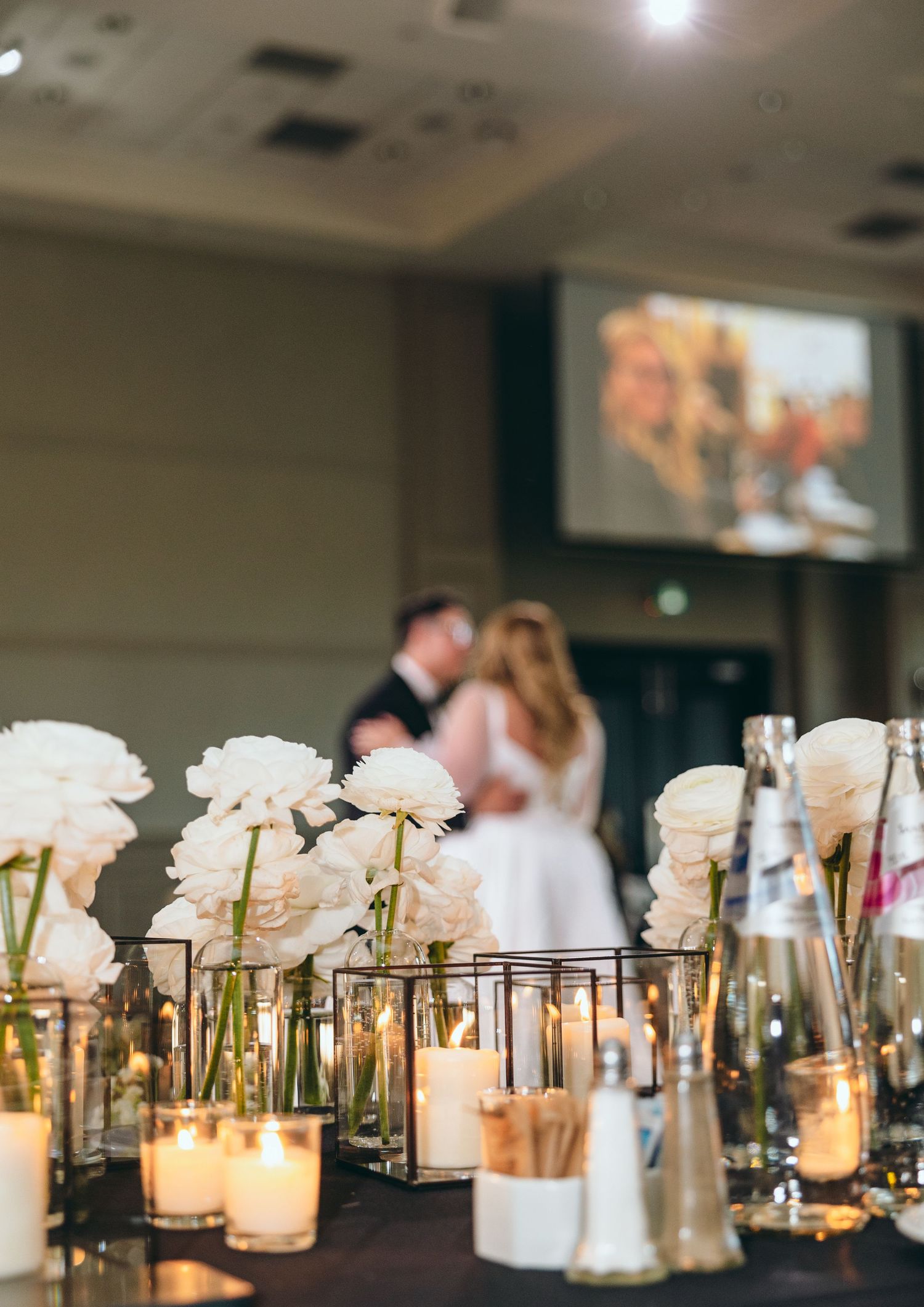 Wedding reception table decorated with white flowers and glowing candles in glass vessels.