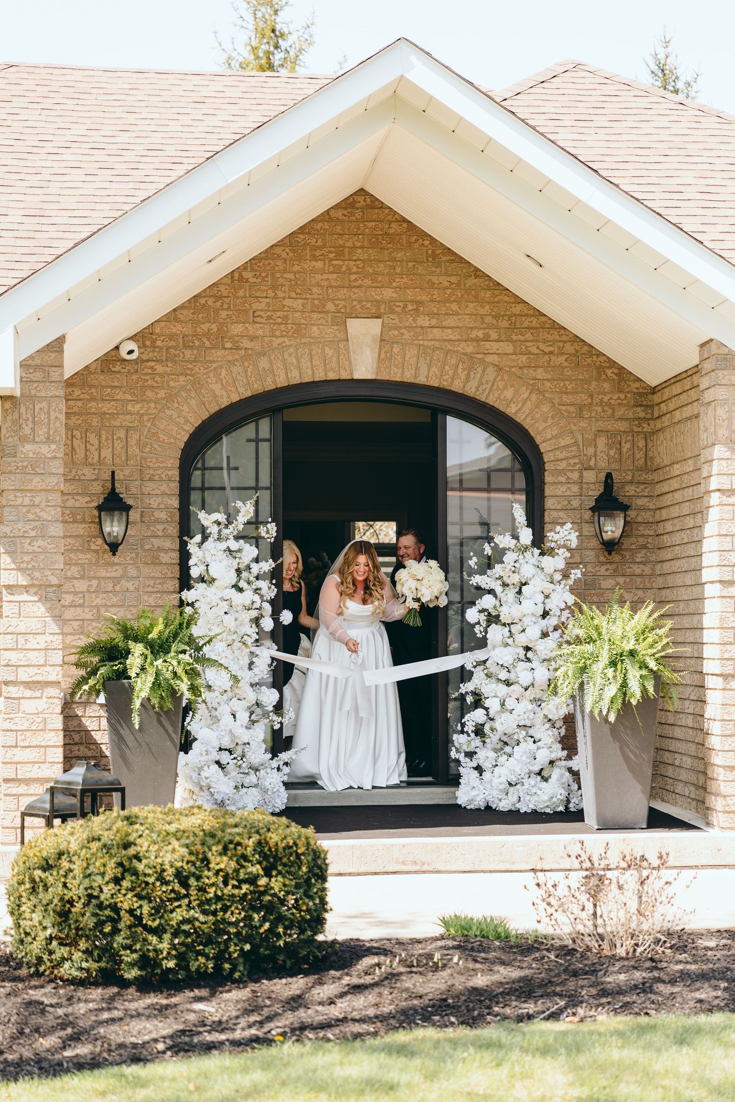 Entrance of a brick house decorated with white floral arrangements for a wedding.